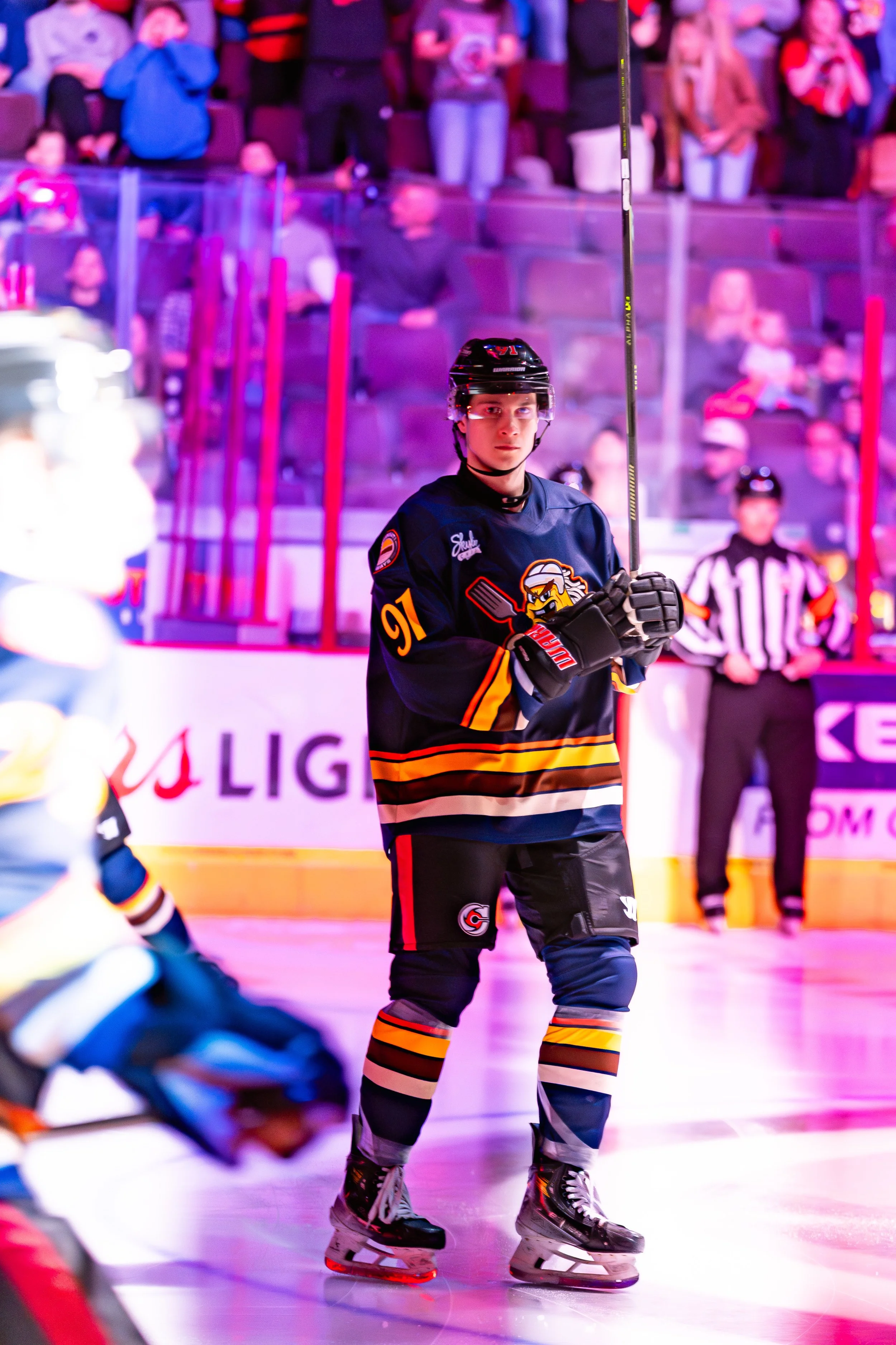 Hockey player in uniform on ice rink, with spectators watching in the background.