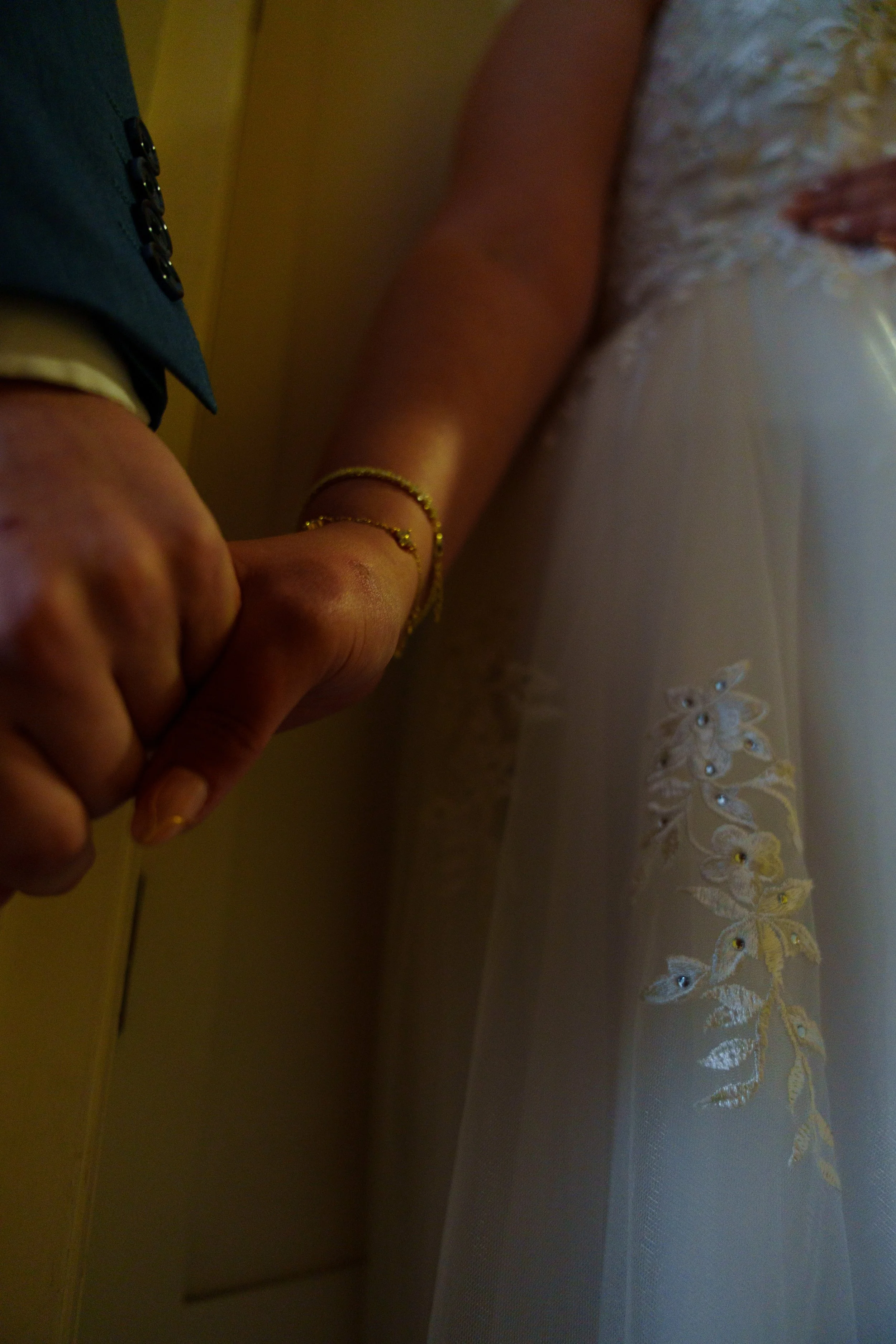 Close-up of a person's hand with a gold bracelet, resting on a white lace fabric with floral embroidery.