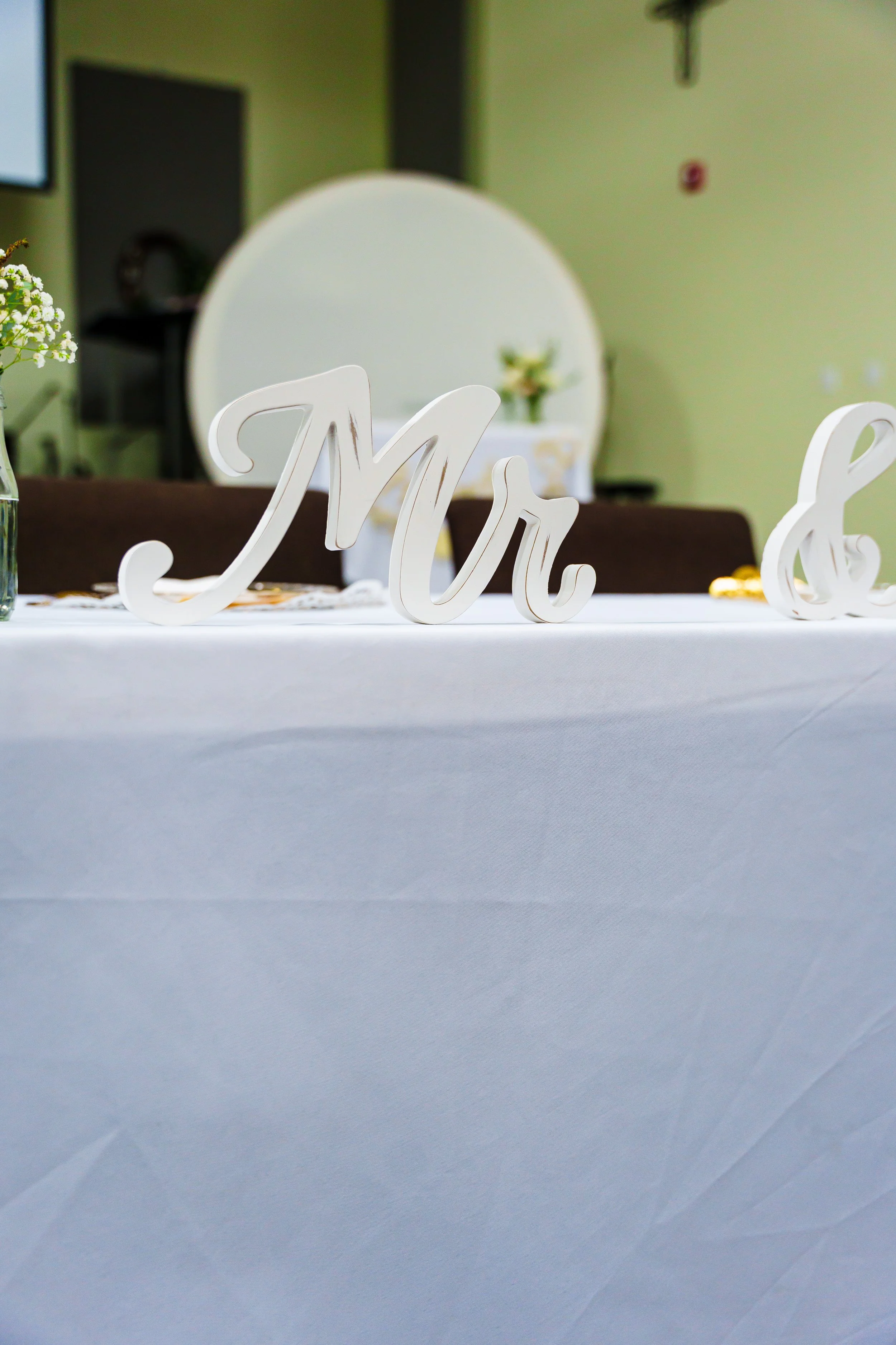 Table decorated with white 'love' sign, flowers, and tablecloth, in a decorated indoor setting
