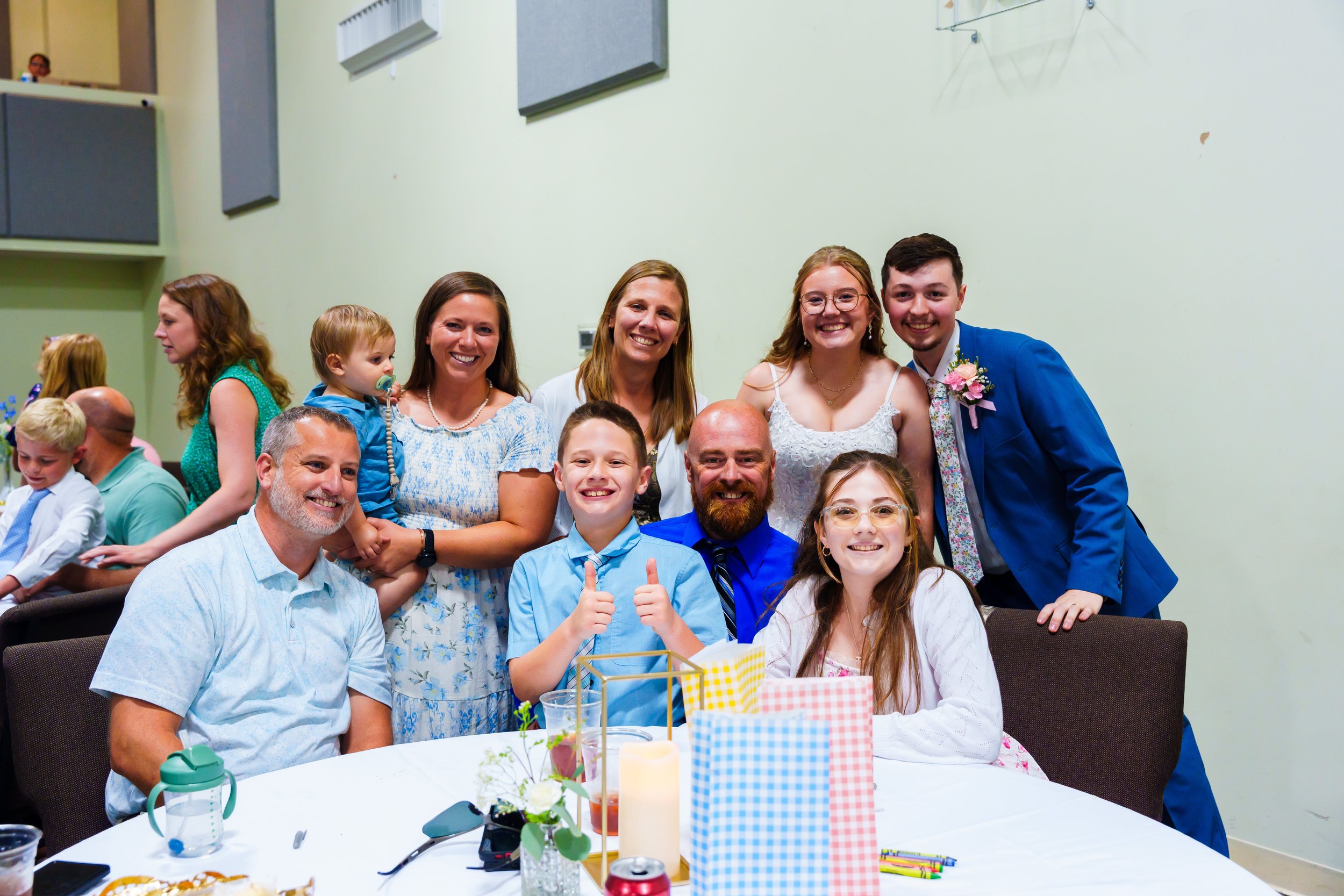 Group of people gathered indoors for a celebration, smiling and posing for a photo, with a decorated table in front.