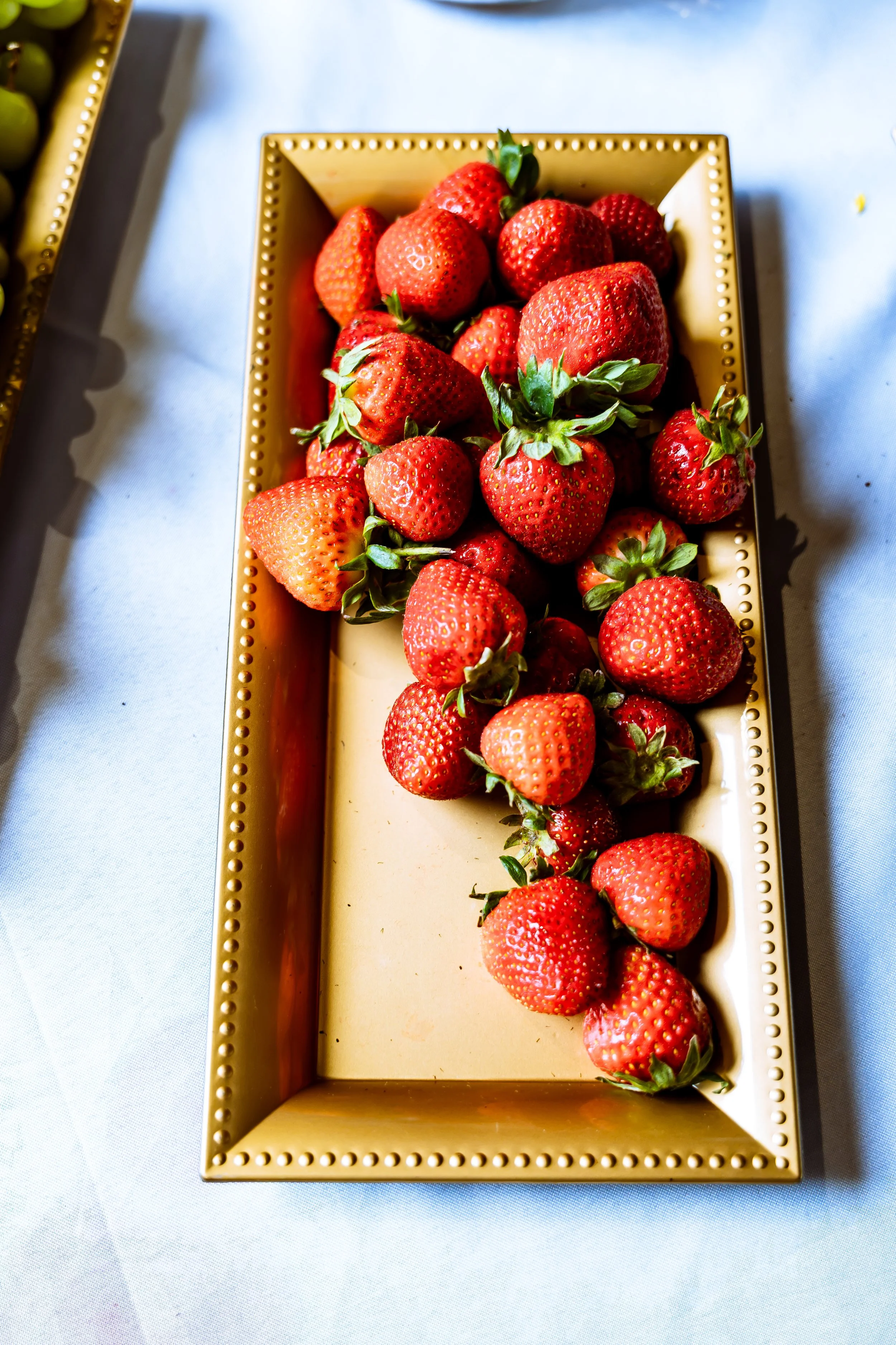 A rectangular beige tray filled with fresh strawberries with green leaves, placed on a light-colored surface.