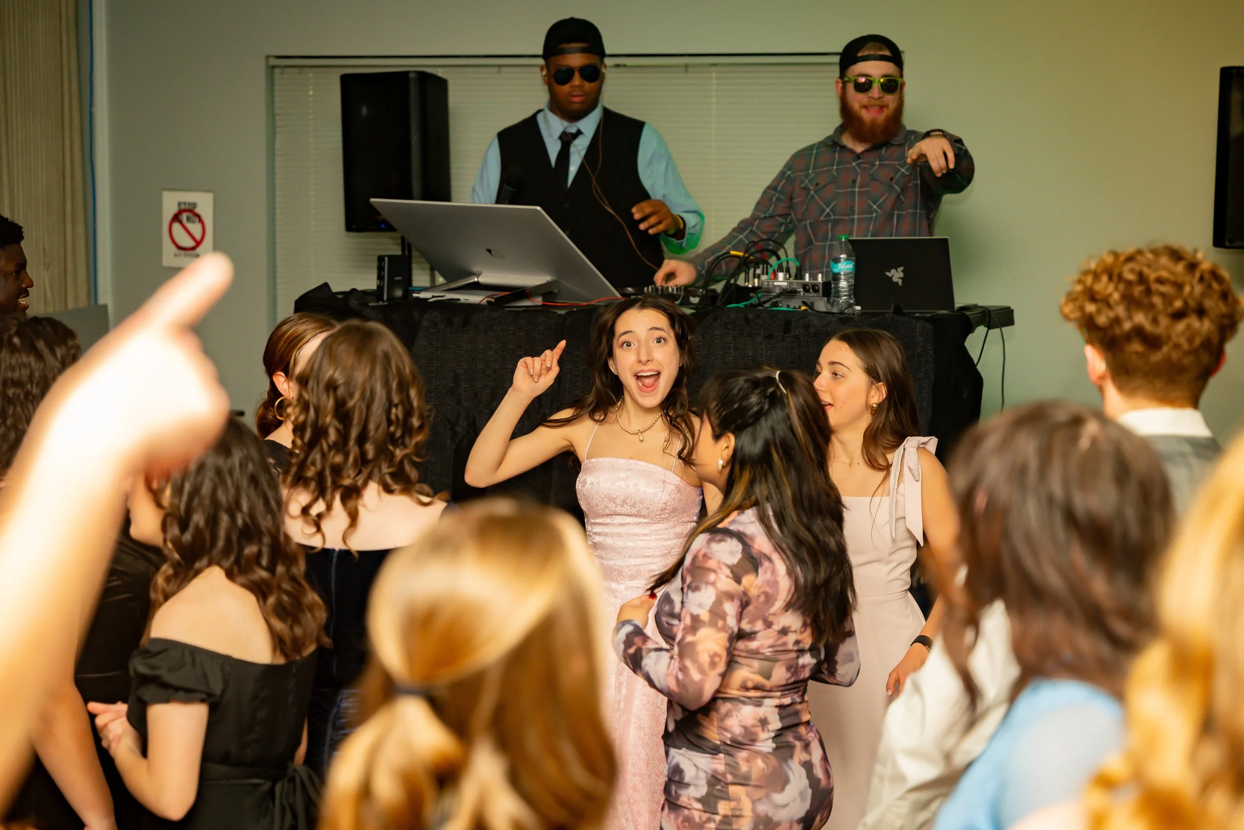 Group of young people dancing and having fun at a party with a DJ in the background.