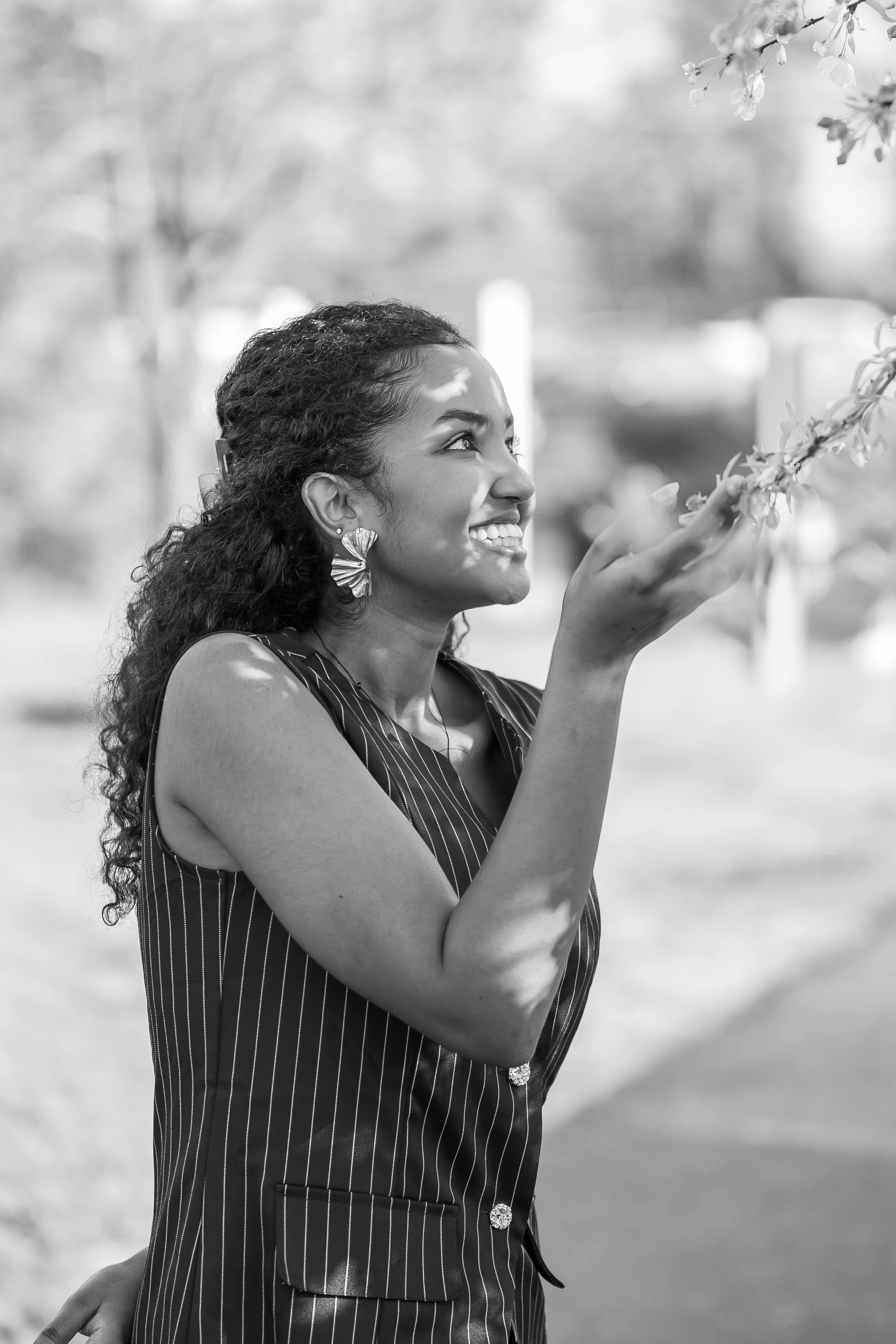A woman smiling and looking at a flower branch outside.