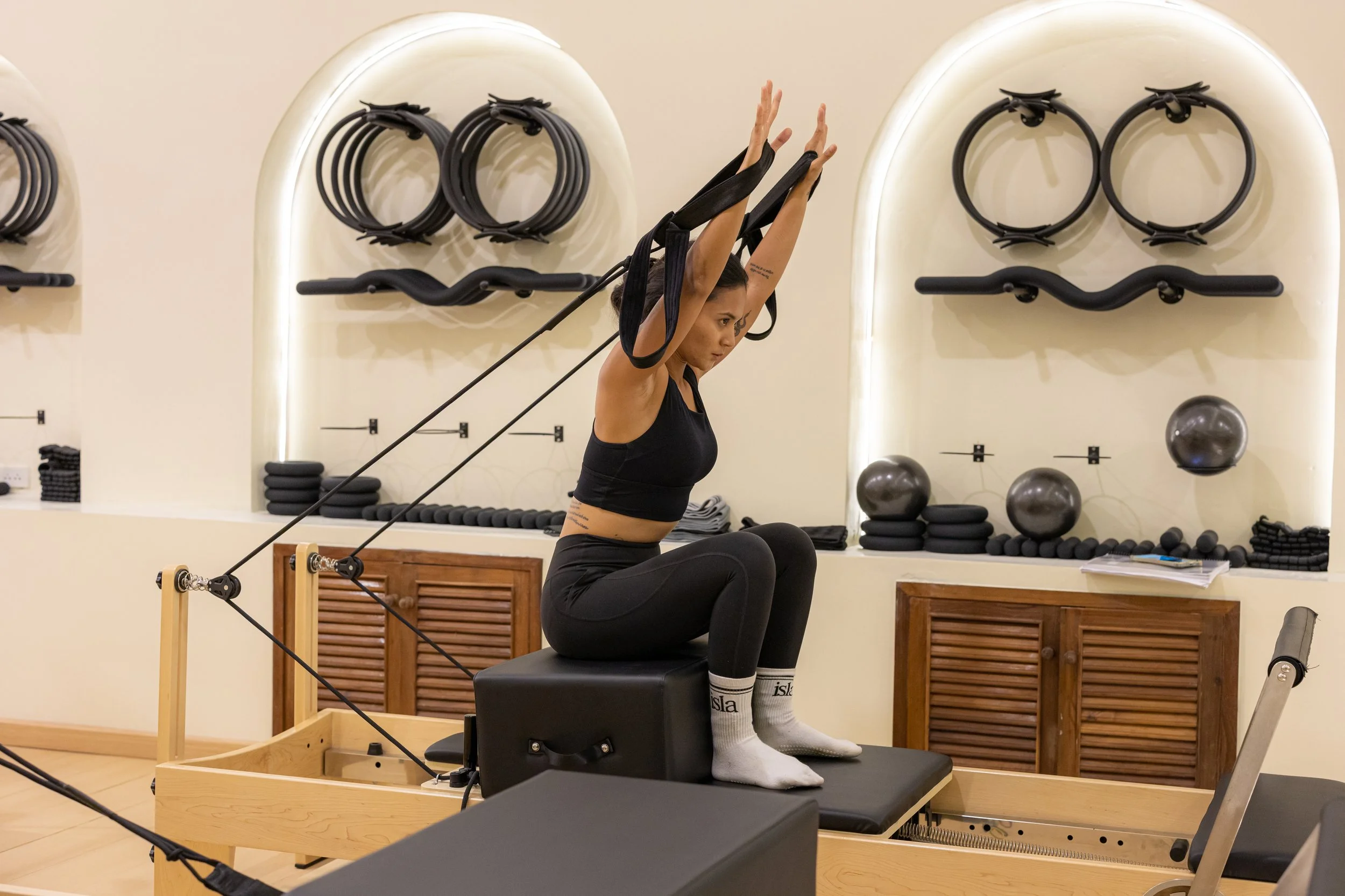 Woman in workout clothes performing an exercise on a Pilates reformer machine, with resistance bands, at Isla Pilates Koh Samui.