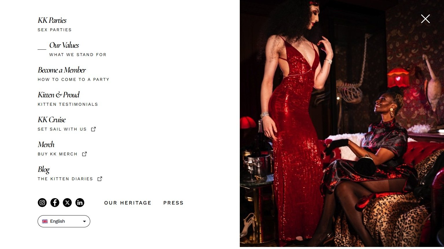 Two women dressed in glamorous, sequined red and black dresses inside a dimly lit, vintage-style lounge. One woman standing and the other seated on a leopard print chaise, both smiling and engaging in conversation.