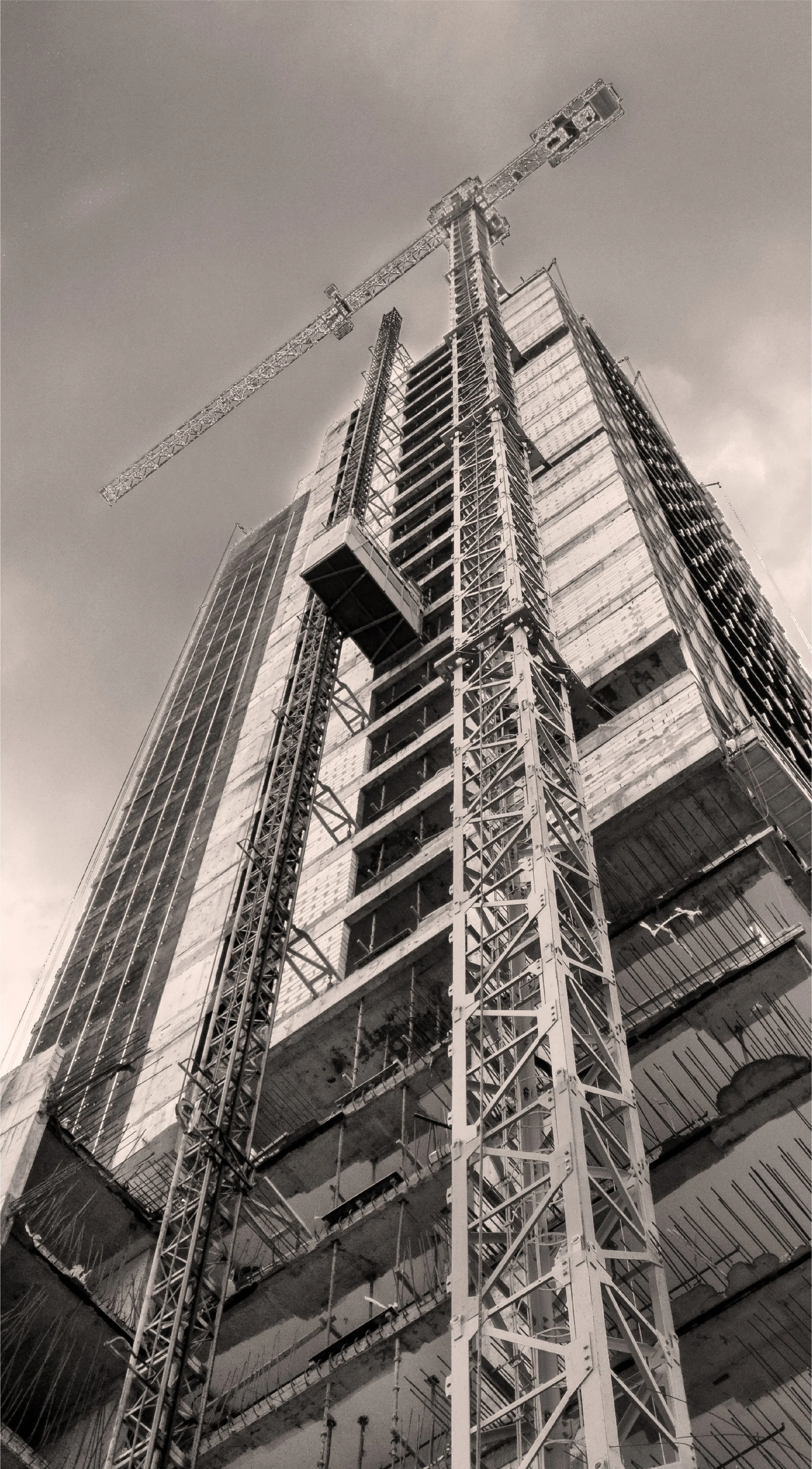 Black and white photo of a tall building under construction, with a crane on top.