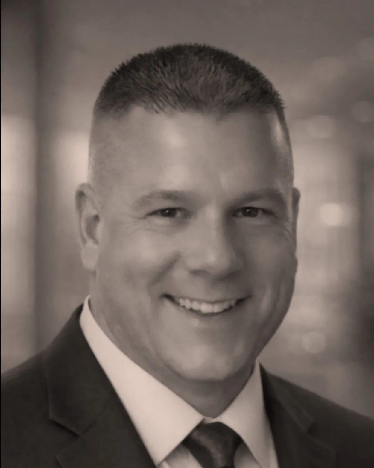 Black and white professional headshot of a smiling man in a suit and tie.