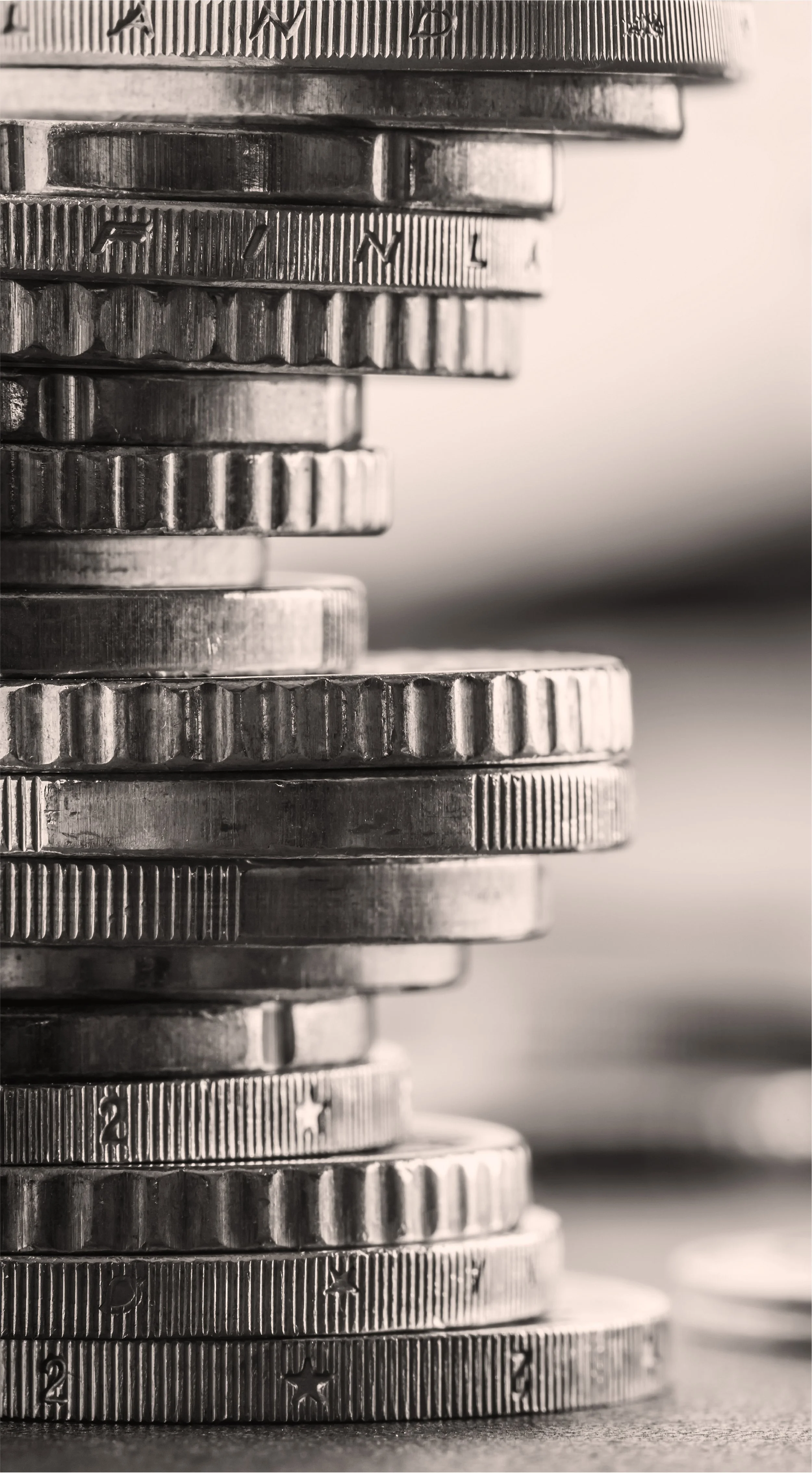 Close-up of stacked silver coins with ridged edges on a flat surface, blurry background.