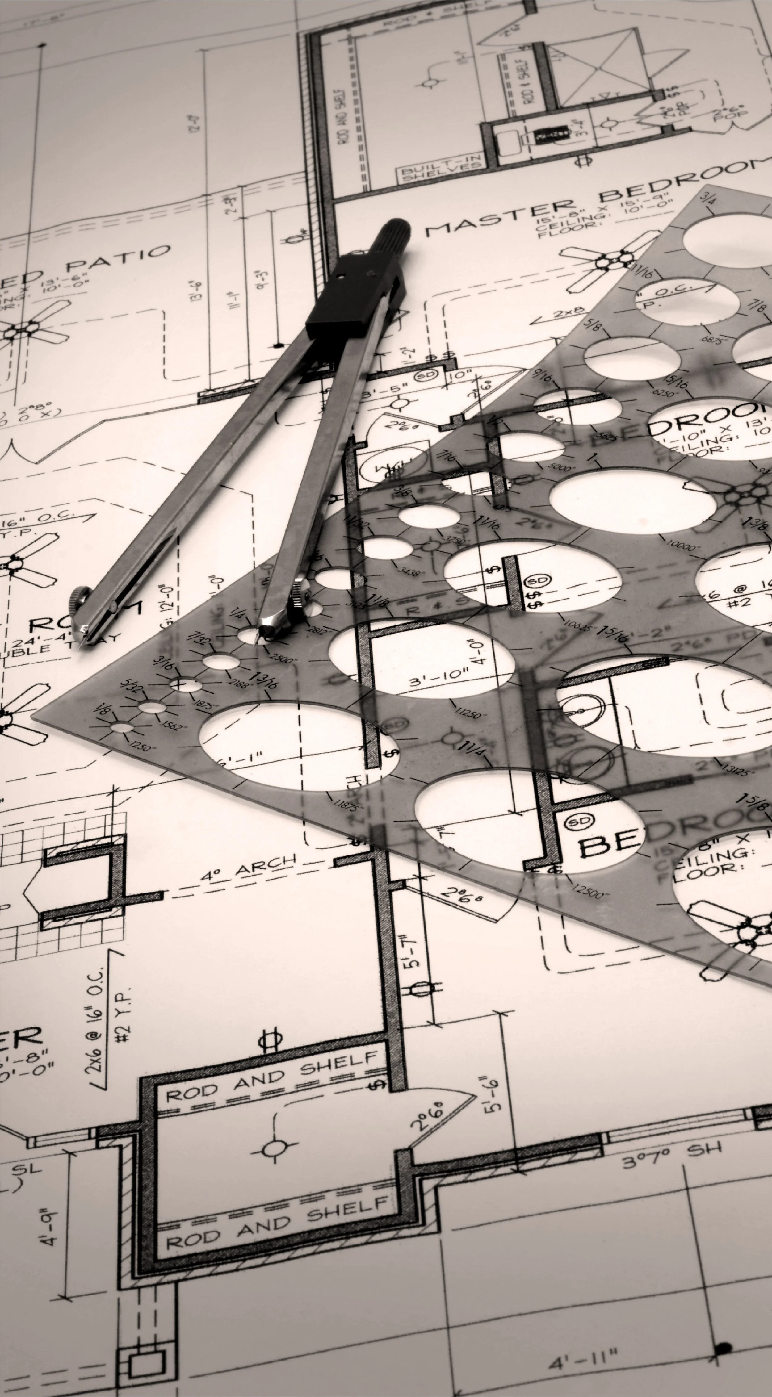 Architectural blueprint with a metal divider and triangle ruler placed on top, showing detailed room layouts and measurements for a house, including master bedroom, bedrooms, patio, and shelving.