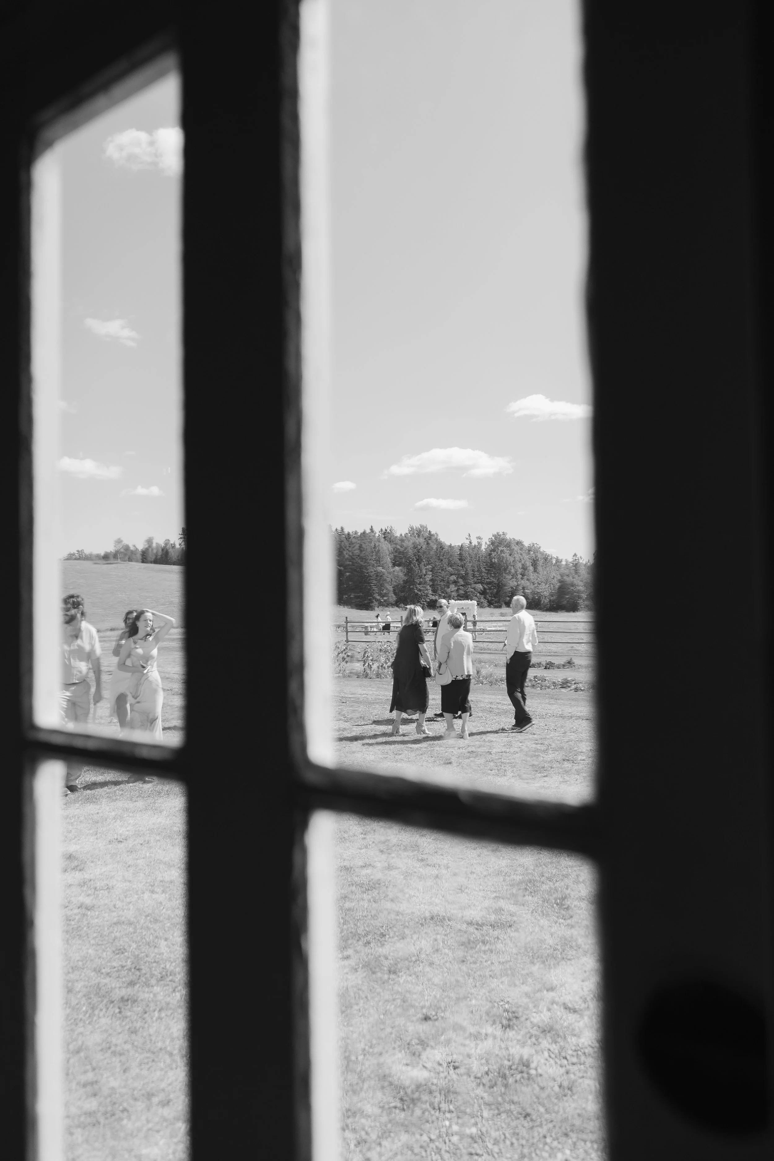 View of people standing outdoors in a field seen through a window with vertical and horizontal bars, in black and white.