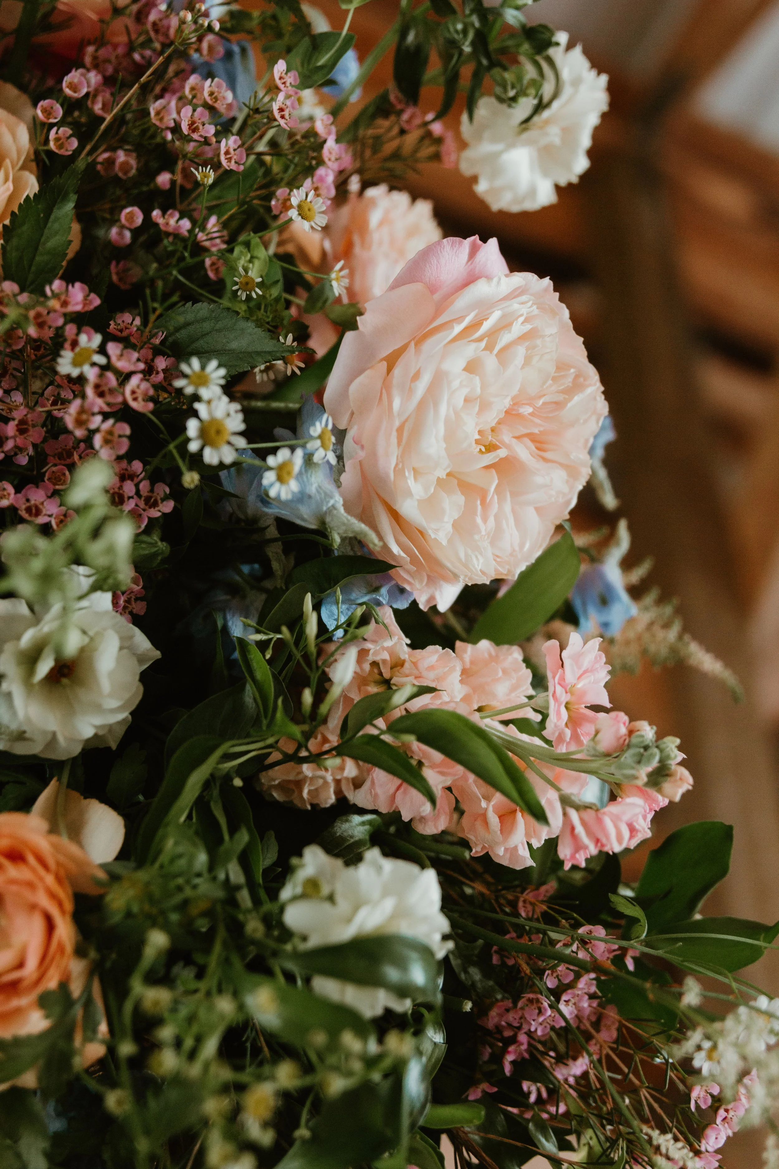 Close-up of a colorful mixed flower bouquet including light pink roses, small white daisies, and pink baby's breath, with green foliage.