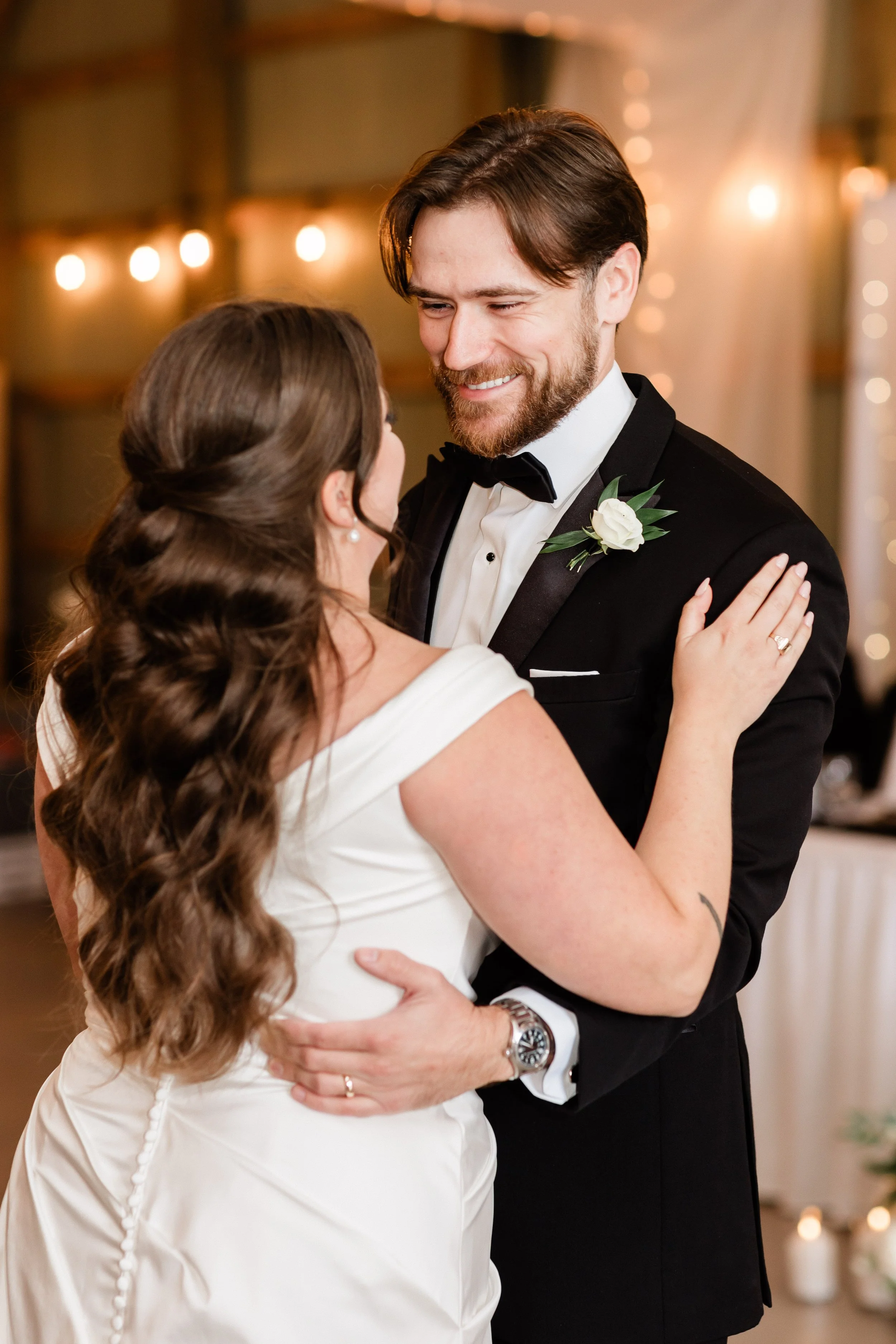 A bride and groom share a dance at their wedding reception, smiling at each other warmly.