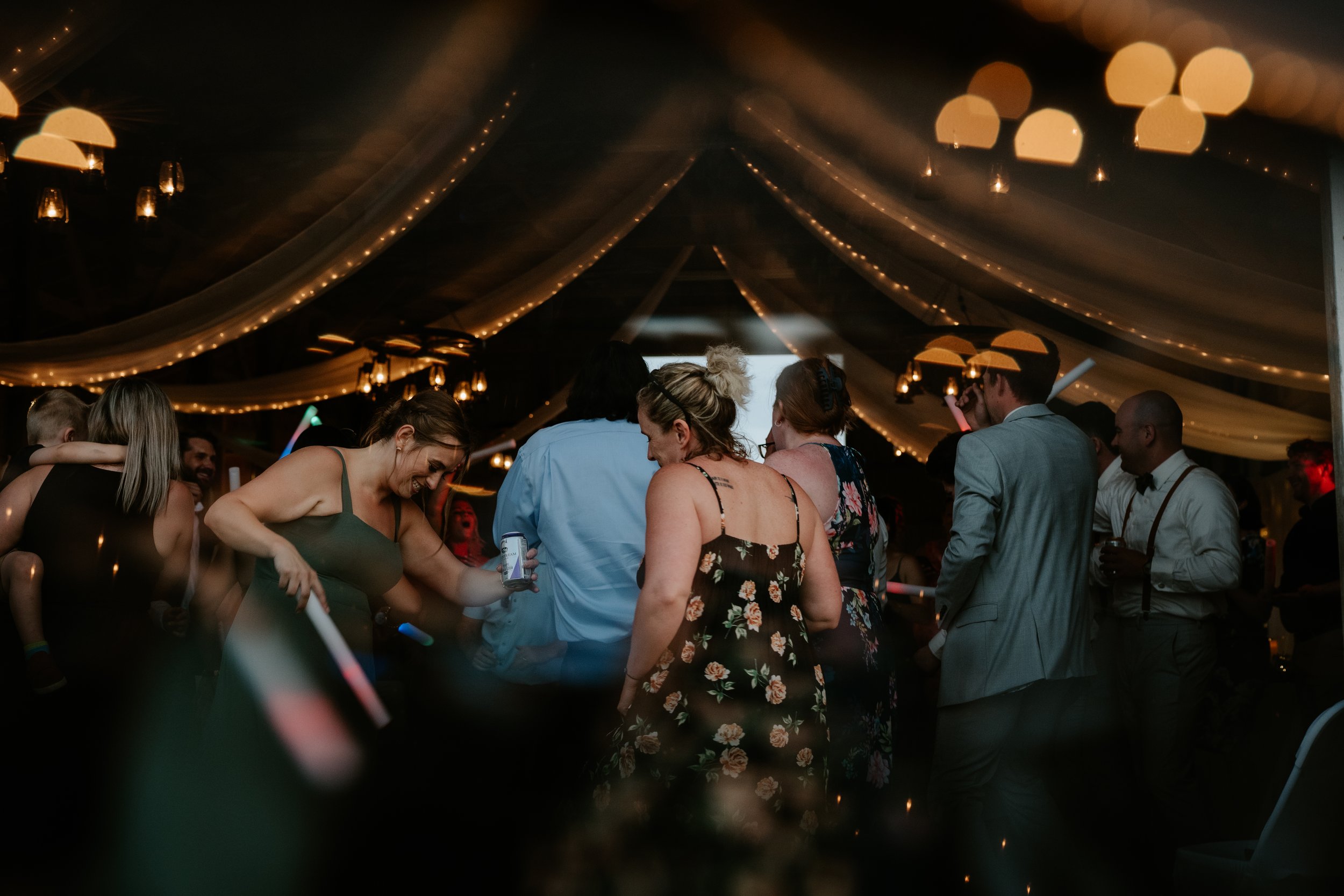 People dancing and socializing at a party under decorated ceiling with string lights and draped fabric.