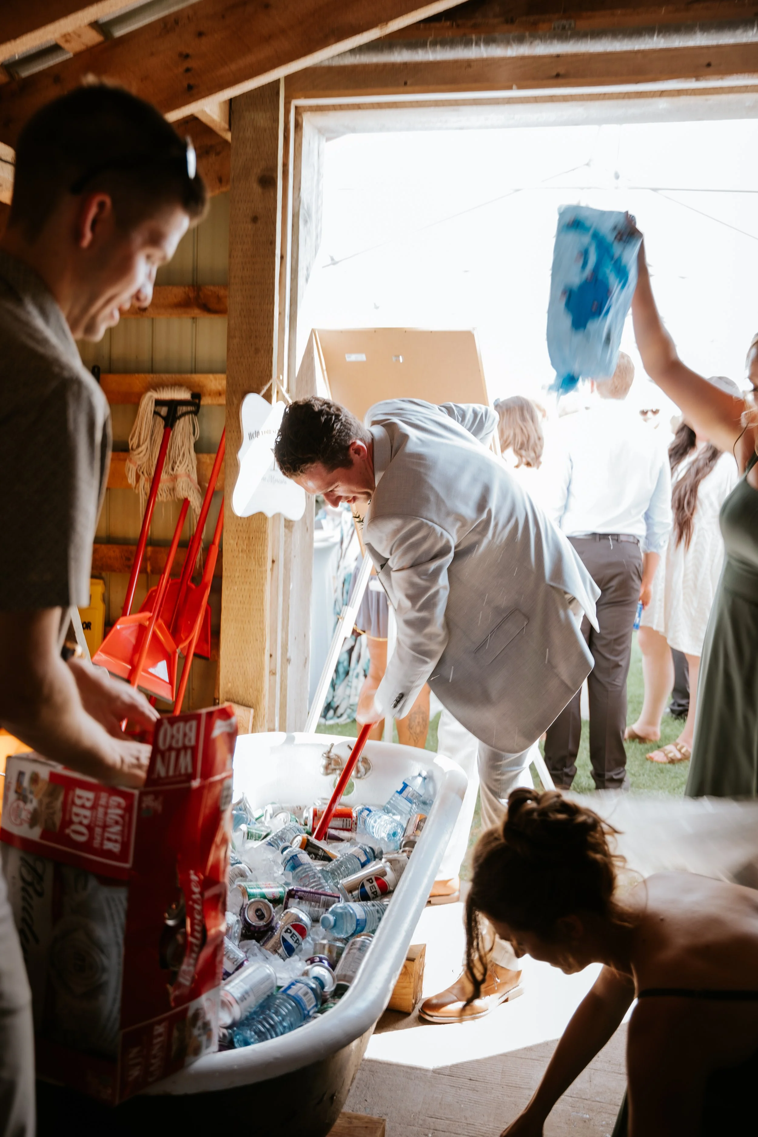 People filling a bathtub with bottles and cans of beverages during an outdoor event, with some individuals standing and others bending down.