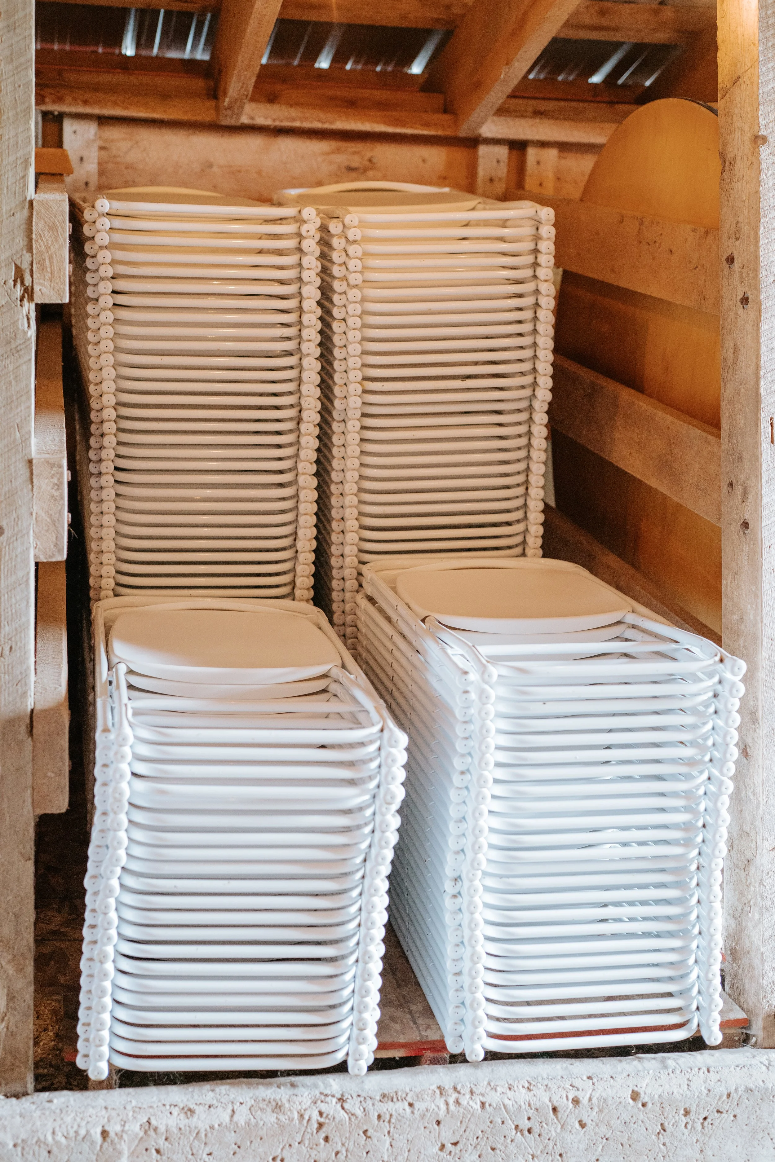 Stacked white plastic chairs in a wooden storage area.