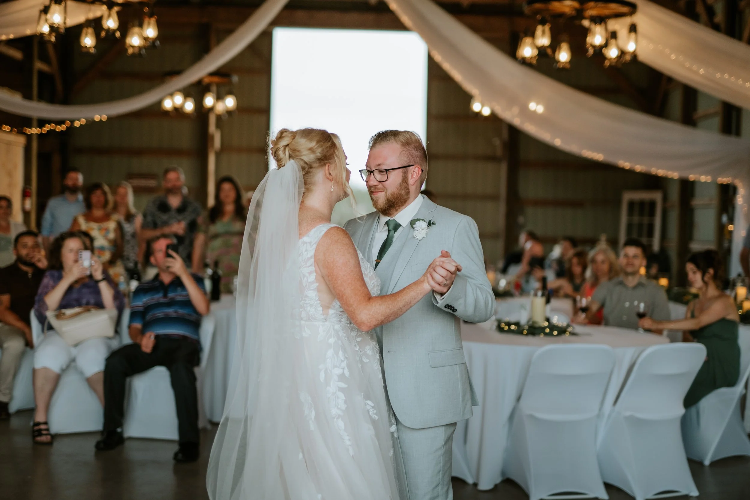 Bride and groom sharing their first dance at wedding reception with guests in background