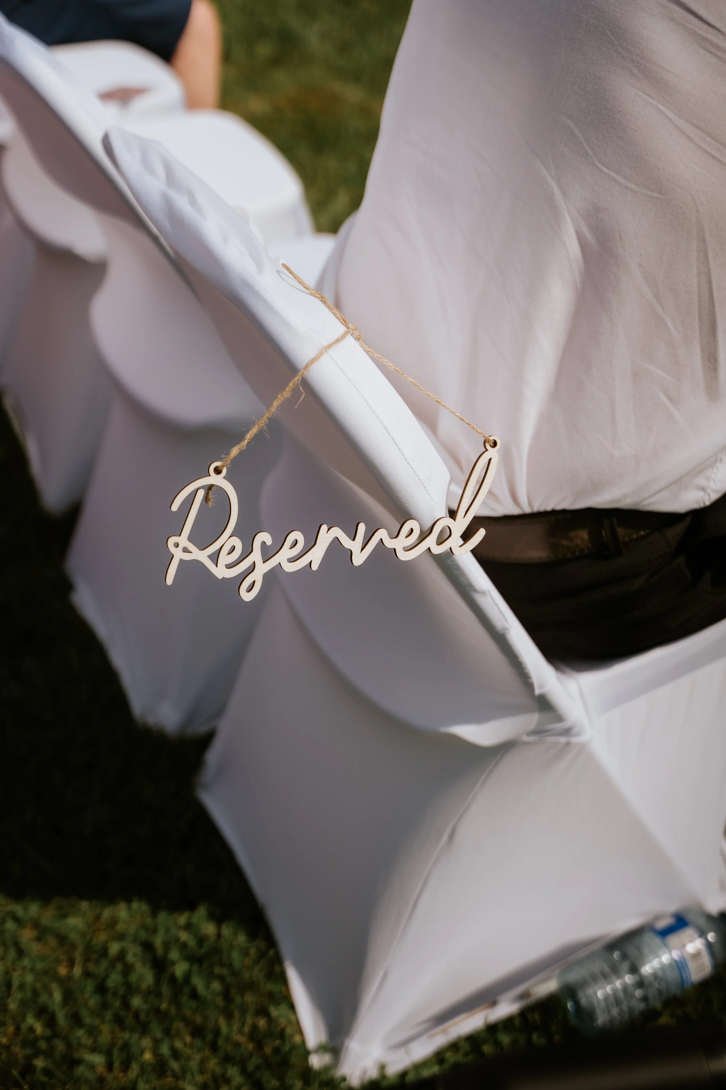 White chair with a "Reserved" sign hanging on its side, set outdoors on grass.