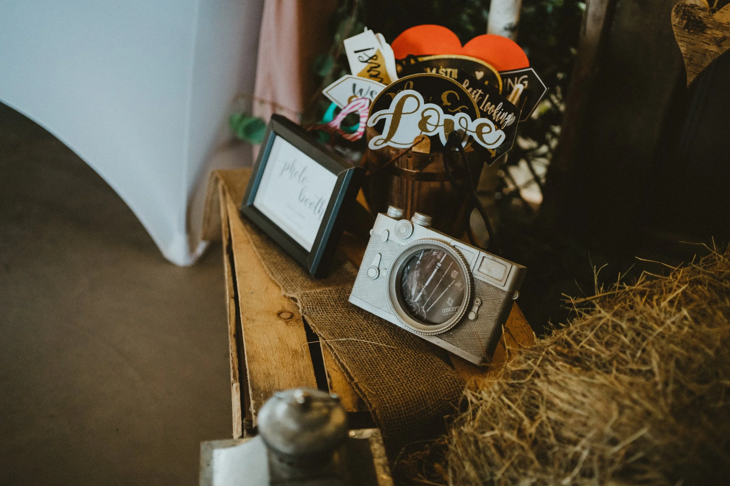 Decorative photo display on a wooden surface, featuring a vintage camera, a framed sign, and a centerpiece with love-themed paper cutouts.