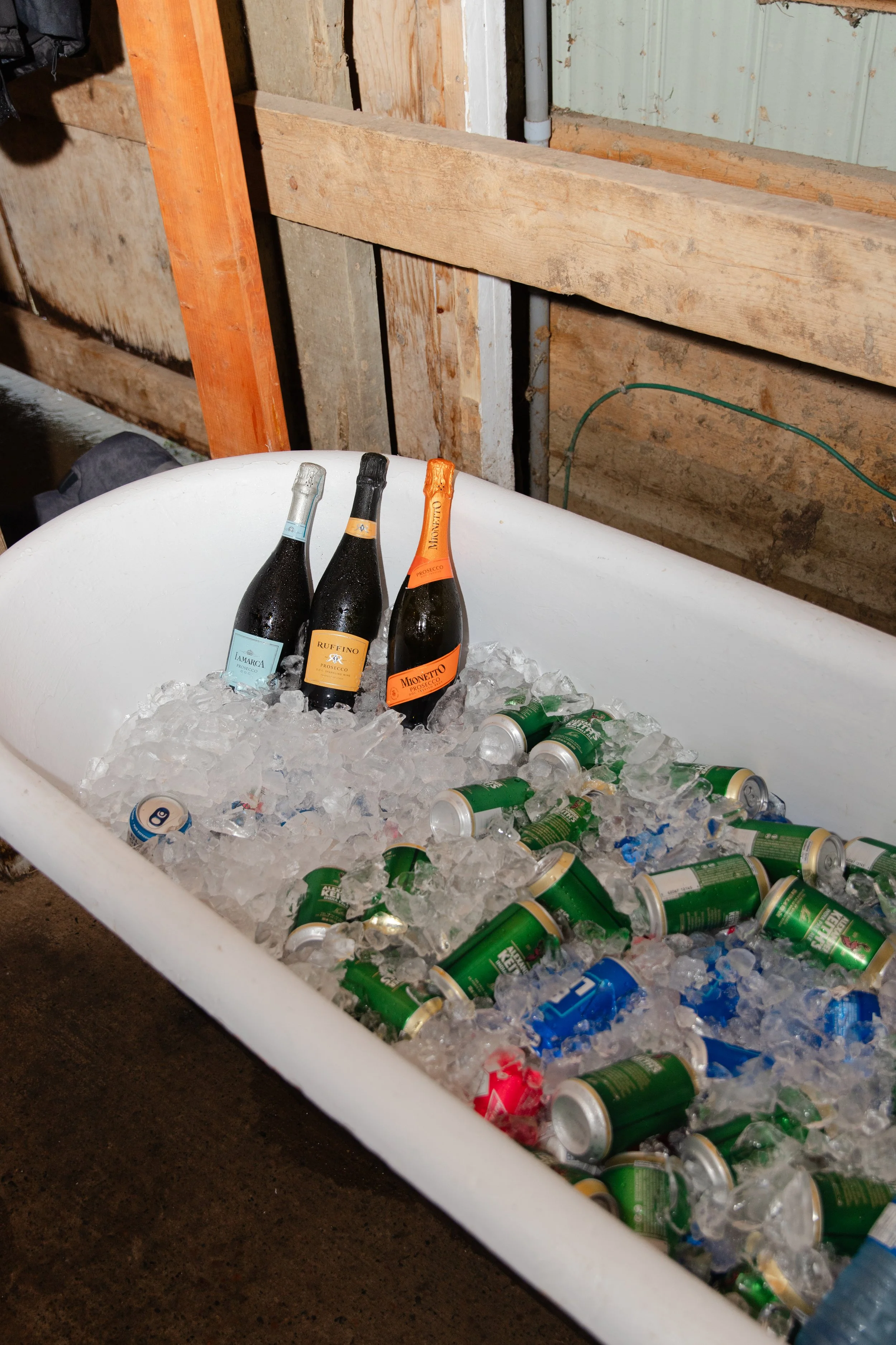 A bathtub filled with ice, holding three bottles of sparkling wine and numerous cans of beverages.