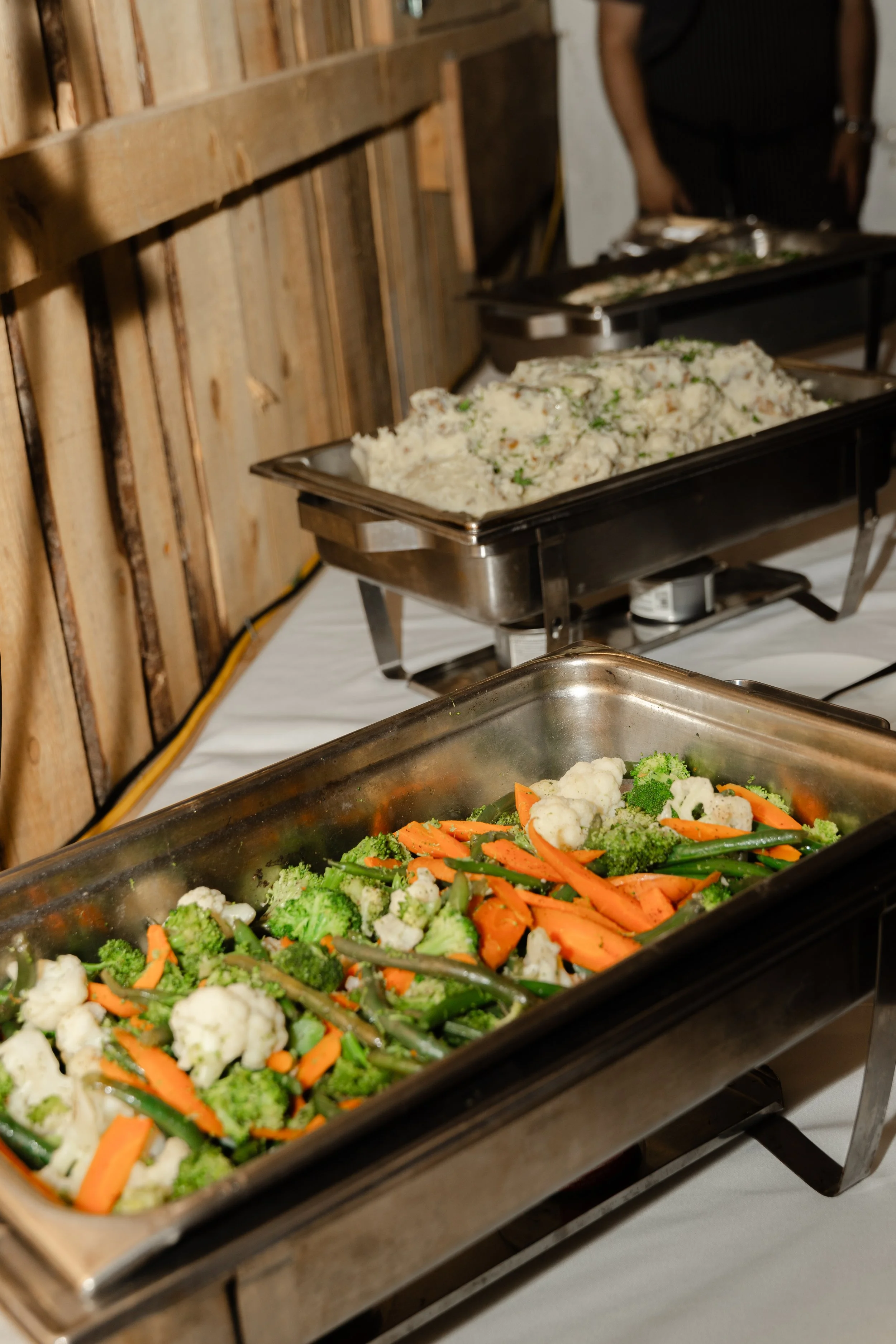 Trays of cooked vegetables, including cauliflower, broccoli, carrots, and green beans, on a buffet table.