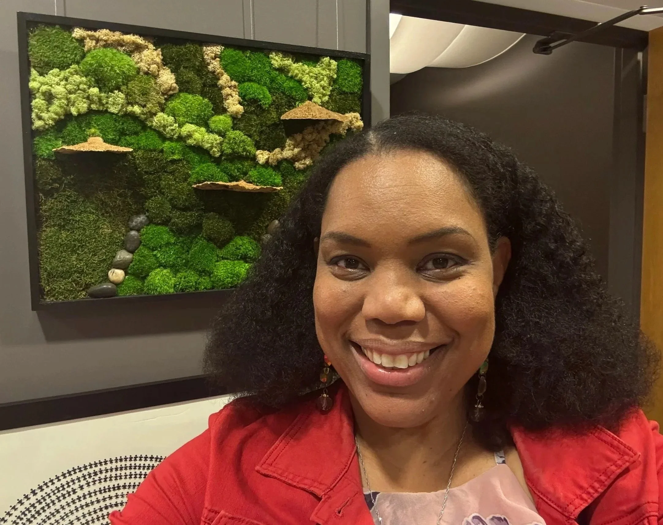 Sekelle Nathan mixed media artist standing in front of Reign a framed moss art panel at the Resonate art exhibit at The Gallery at Morningstar art gallery