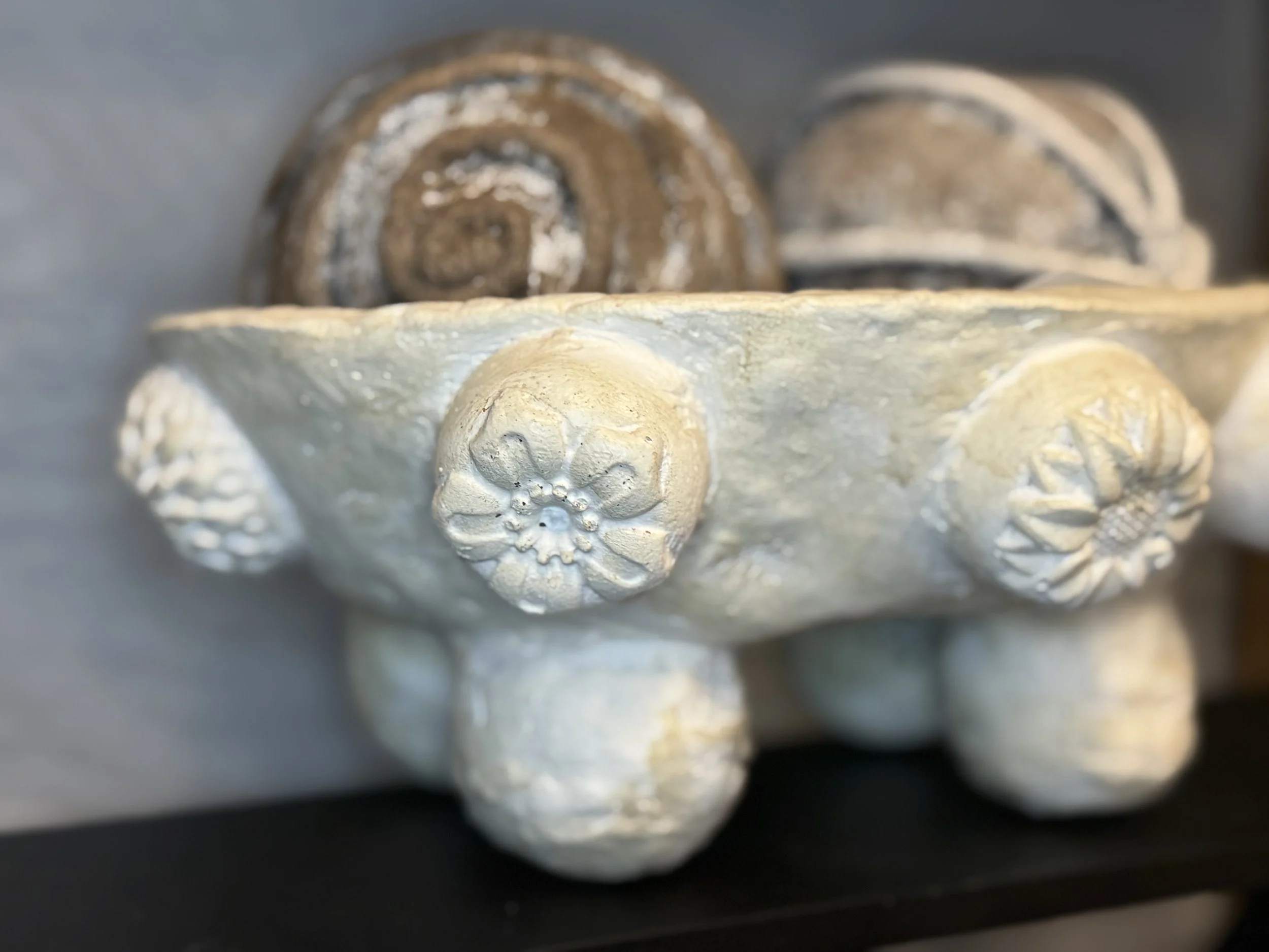 Close-up of a ceramic decorative object with floral and swirl patterns in a light color, with darker, spiral-patterned objects in the background.