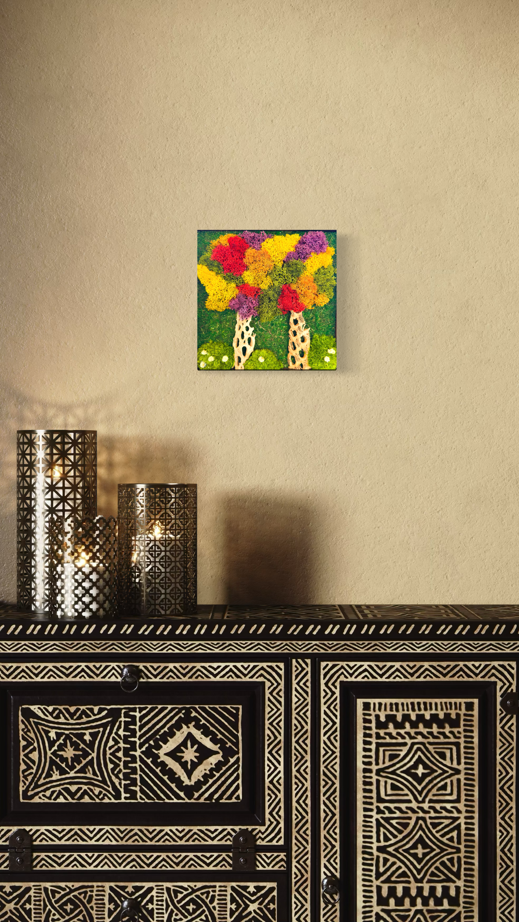 Colorful wall art of two trees with vibrant, multicolored foliage above a black and white patterned cabinet, with decorative candles in metallic holders on a table below.