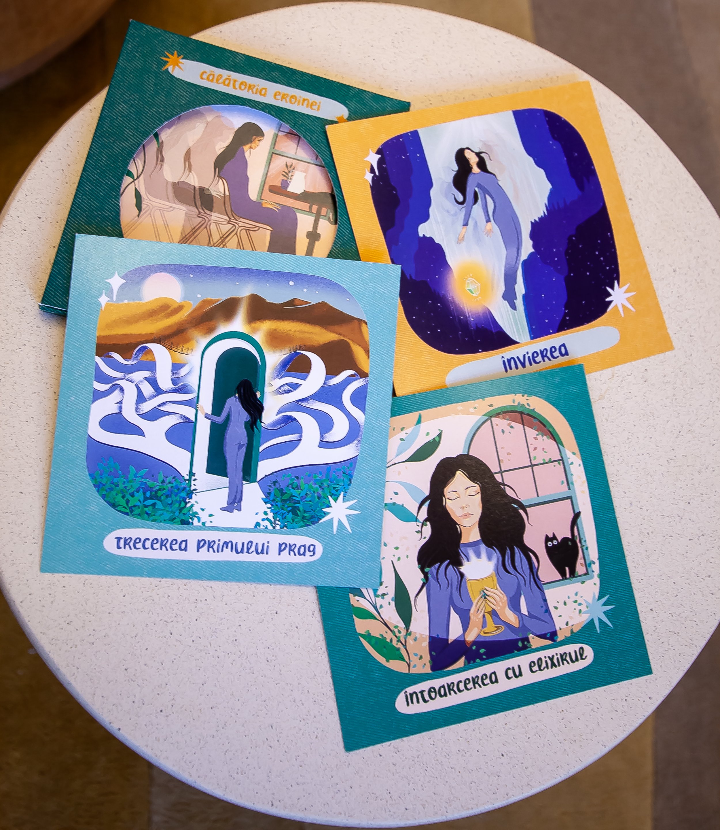 Four illustrated oracle cards on a white table, each depicting a different scene with a woman and symbols, with Romanian text. - Carduri Calatoria Eroinei