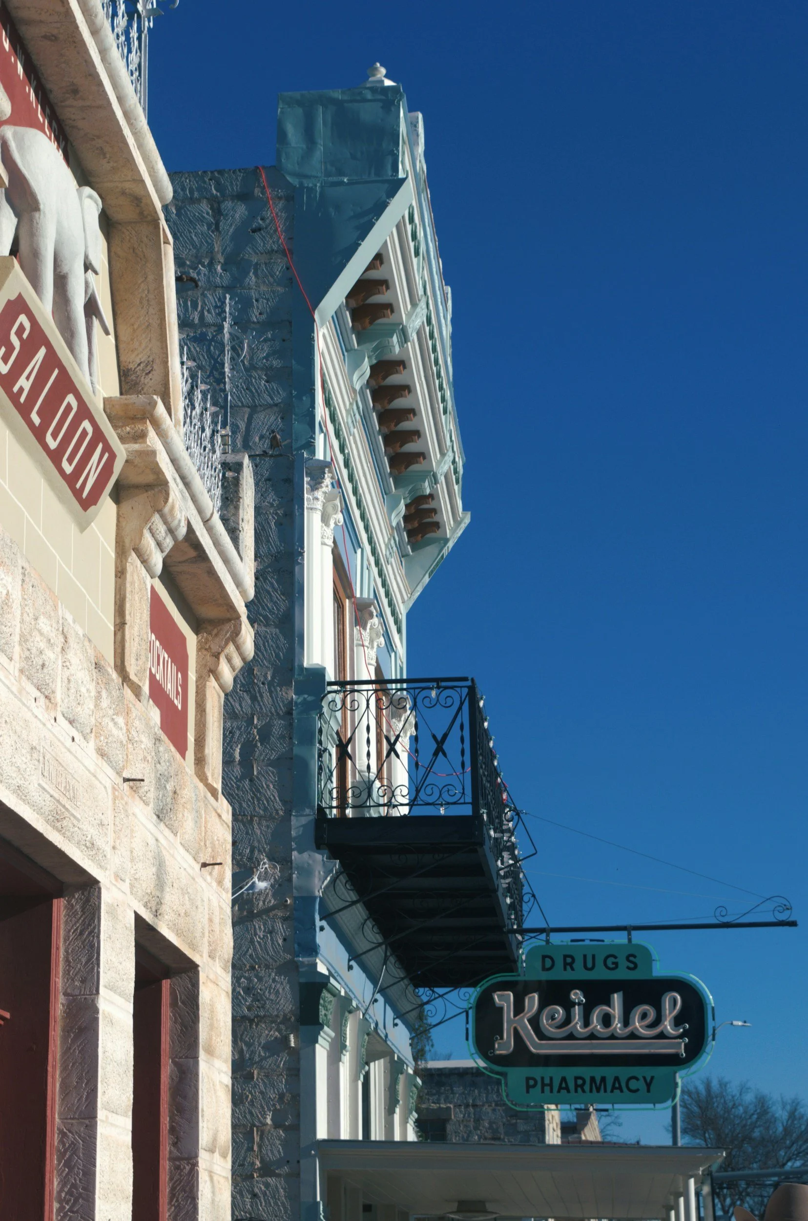A historic building with a sign for a pharmacy called Keidel, with additional signs for drugs and pharmaceuticals, ascending in a sunny setting with a clear blue sky.