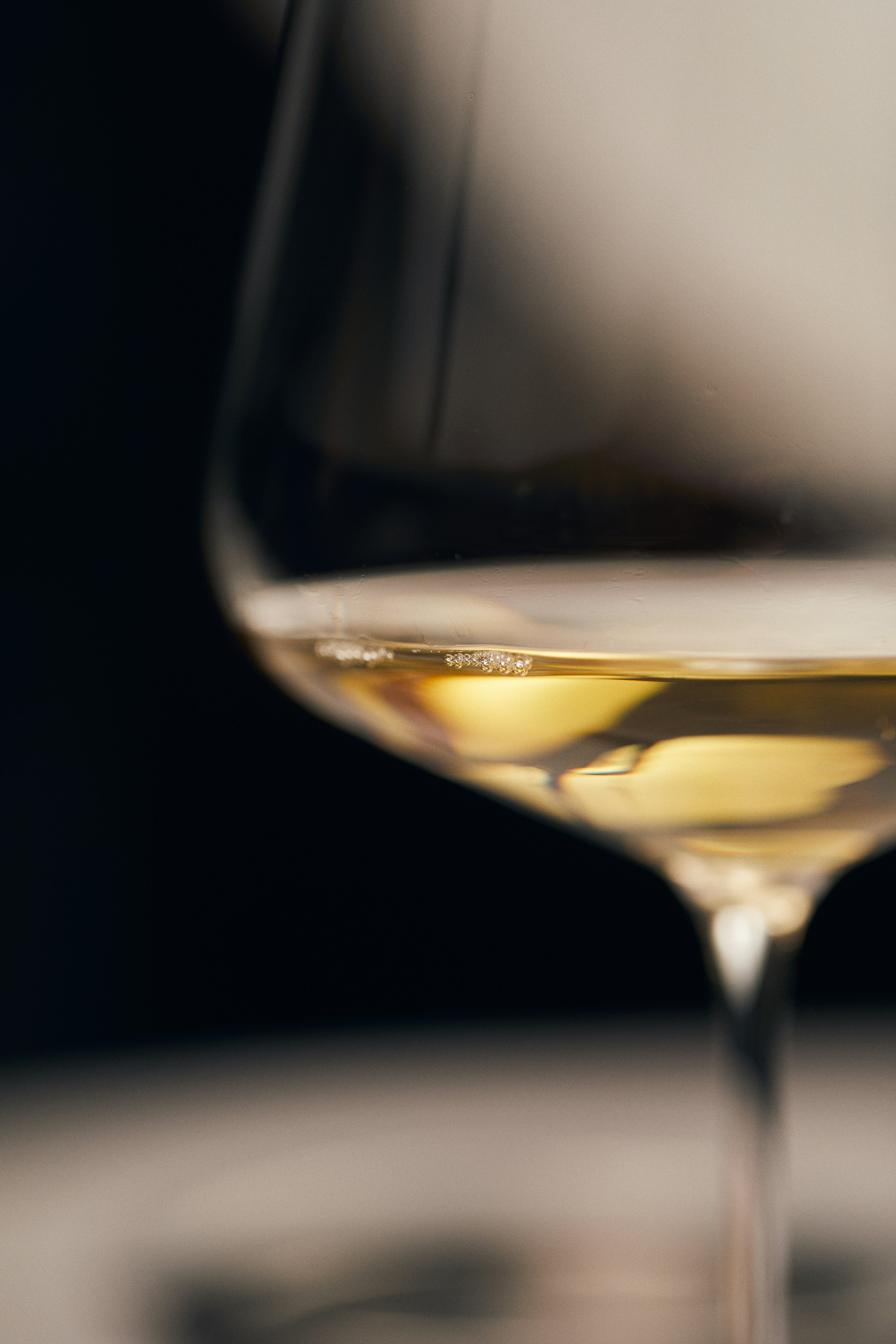 Close-up of a glass of white wine with bubbles, against a dark background.