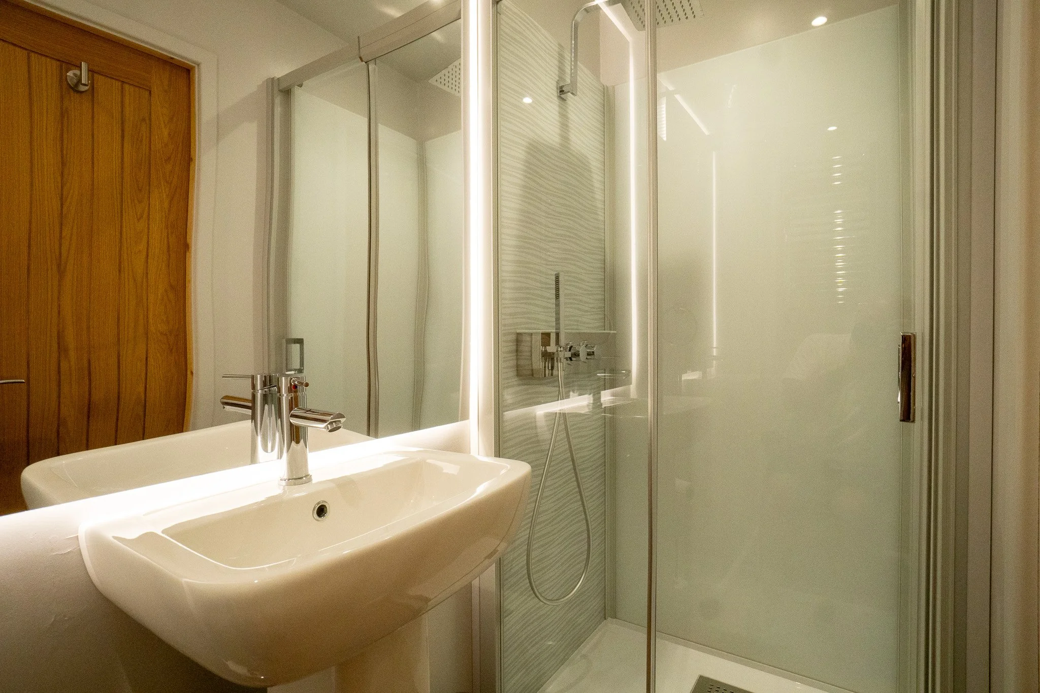 Modern bathroom with a white sink, a wooden door, and a glass shower enclosure with a sleek, minimalist design.