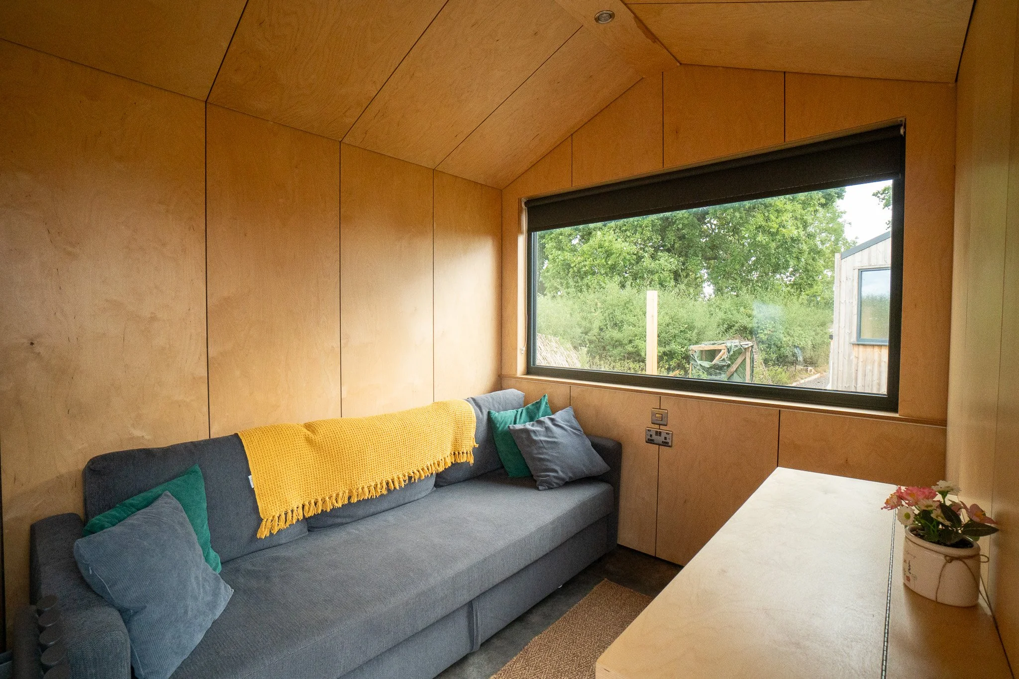 A small cozy room with wooden paneled walls and a large window showing a view of trees