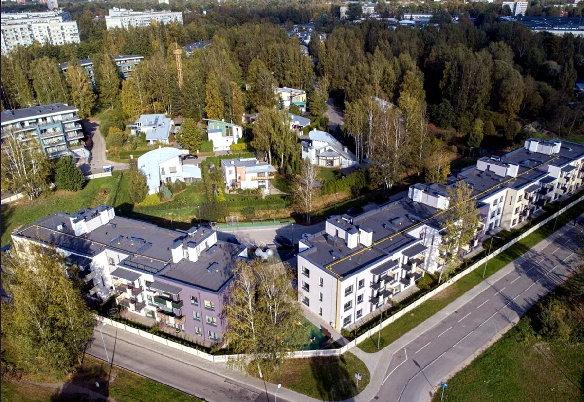 Aerial view of a residential neighborhood with modern apartment buildings, houses, and a wooded area in the background.