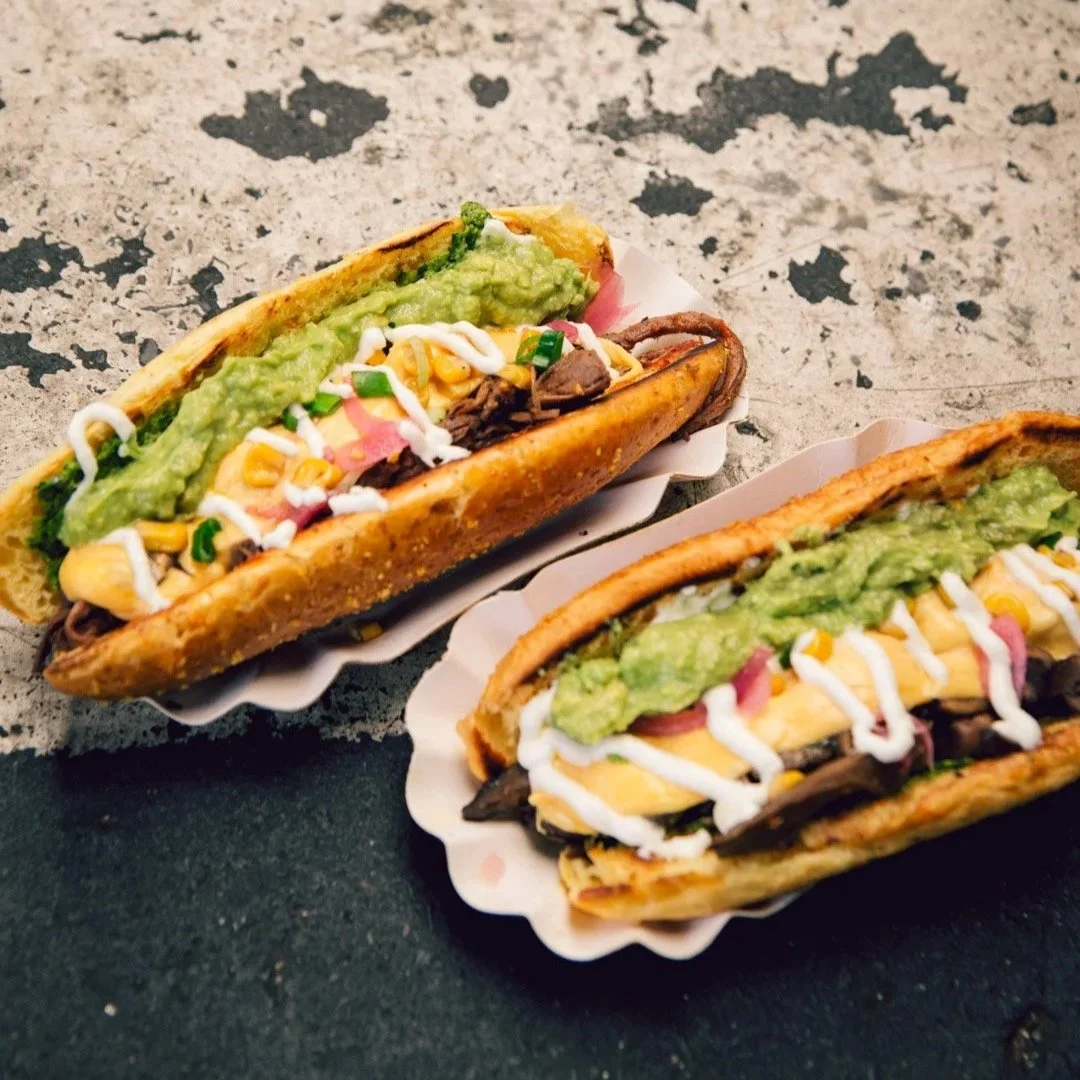 zwei Sandwiches in weißen Schalen liegen auf einer betonierten Oberfläche. Die Sandwiches sind belegt.