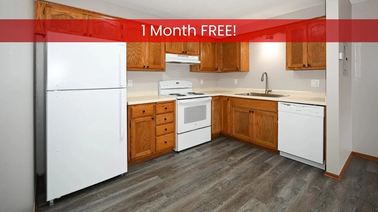 Apartments in Austin MN: Kitchen with wood cabinets, white appliances, and gray flooring. Text reads 1 Month FREE! across the top.