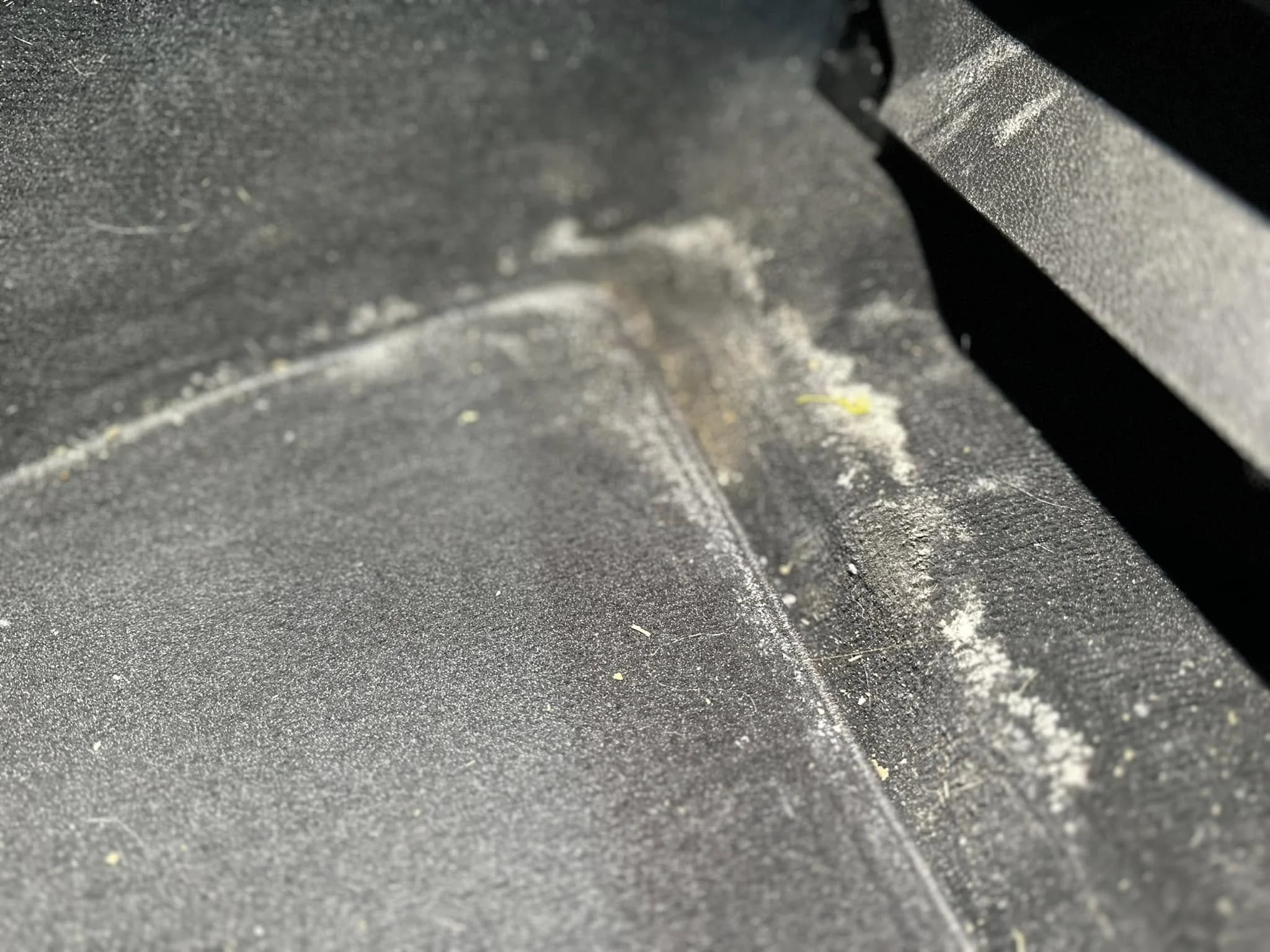 Close-up of a dusty, black textured surface with some dirt and debris scattered on it.