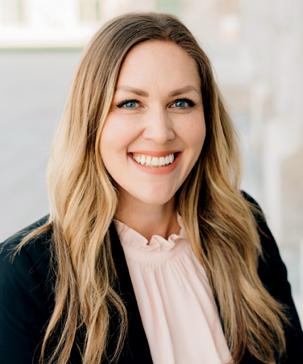 A smiling woman with long blonde hair wearing a black blazer and light pink blouse.