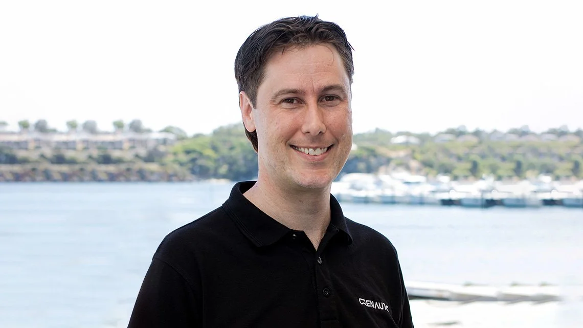 Man smiling outdoors near water with boats in background