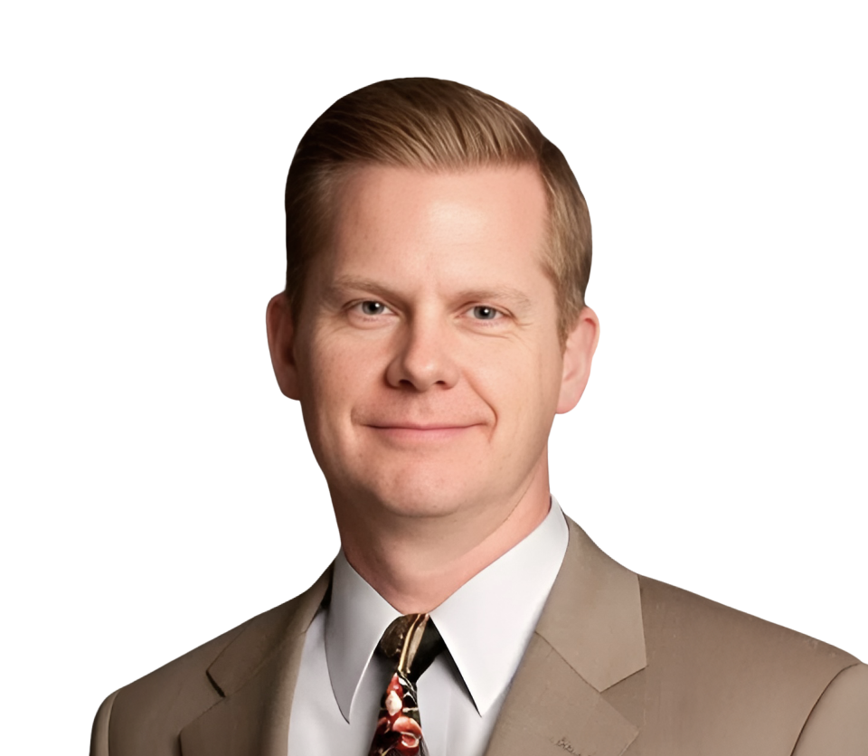 A young man with light skin and blonde hair, wearing a beige suit, white shirt, and floral tie, smiling against a plain white background.