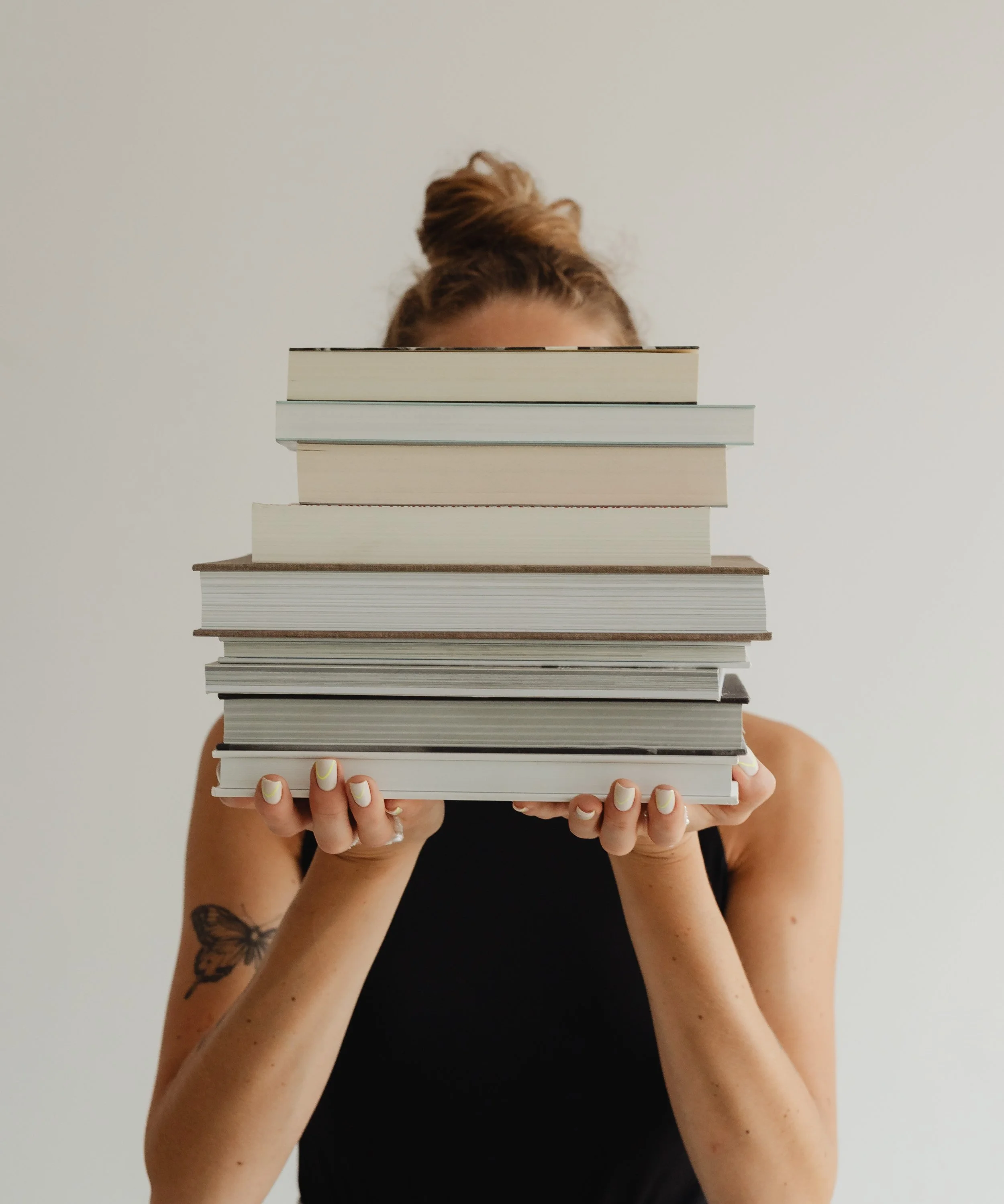 Person holding a large stack of books covering their face