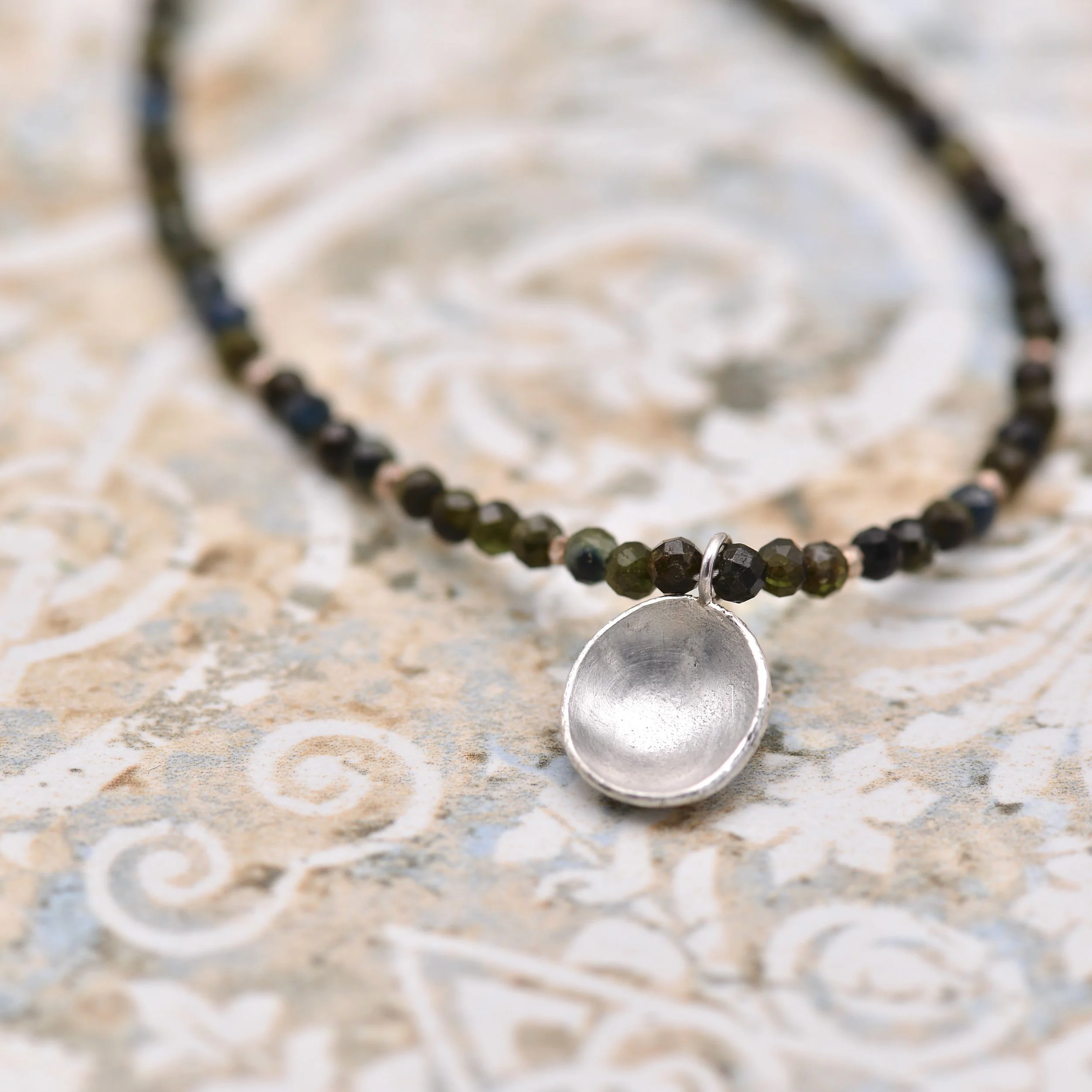 Close-up of a silver domed pendant with Black Tourmaline faceted gemtones on a textured surface.