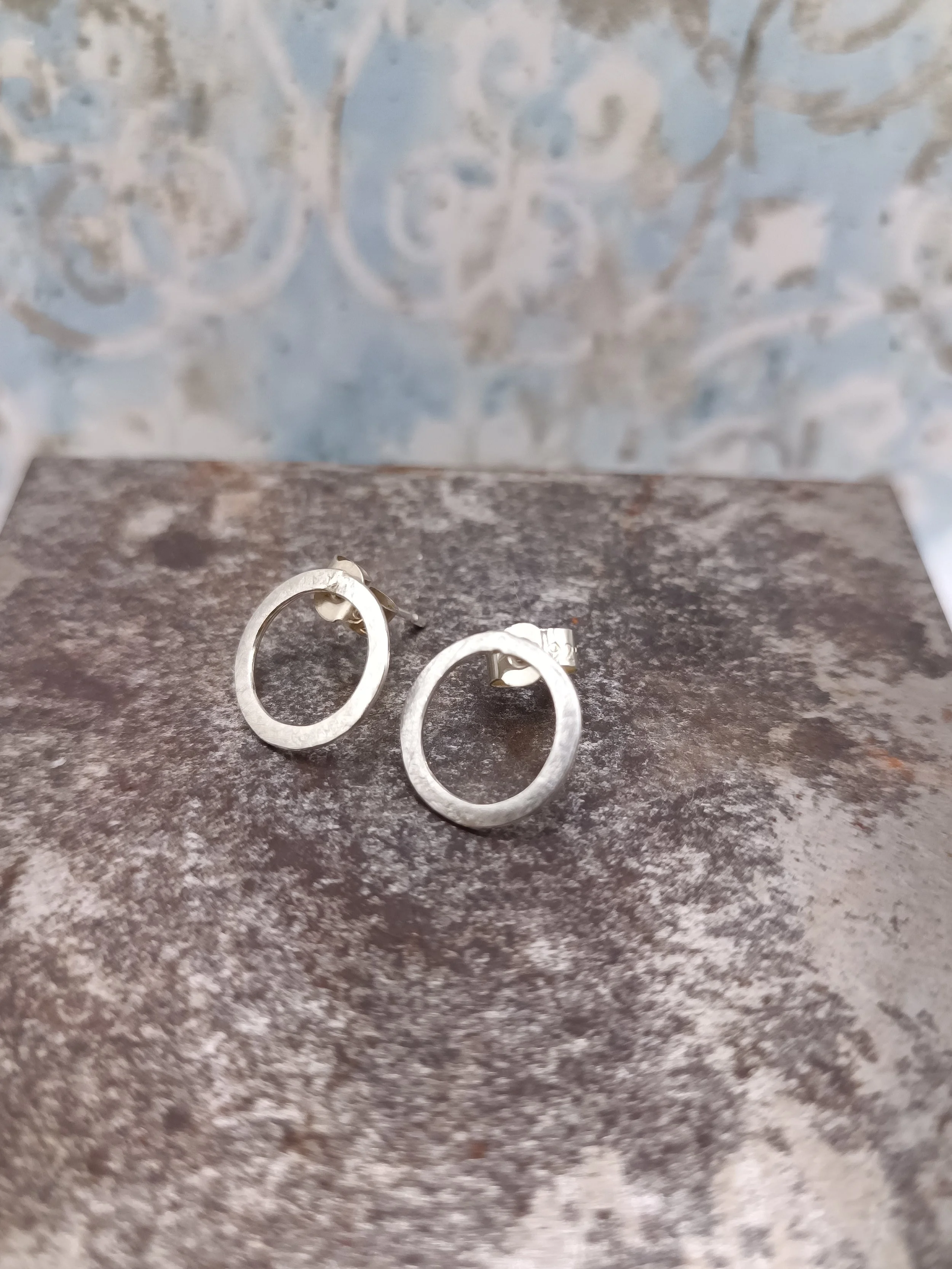 Close-up of silver hoop earrings on a textured dark surface with a blurred background.