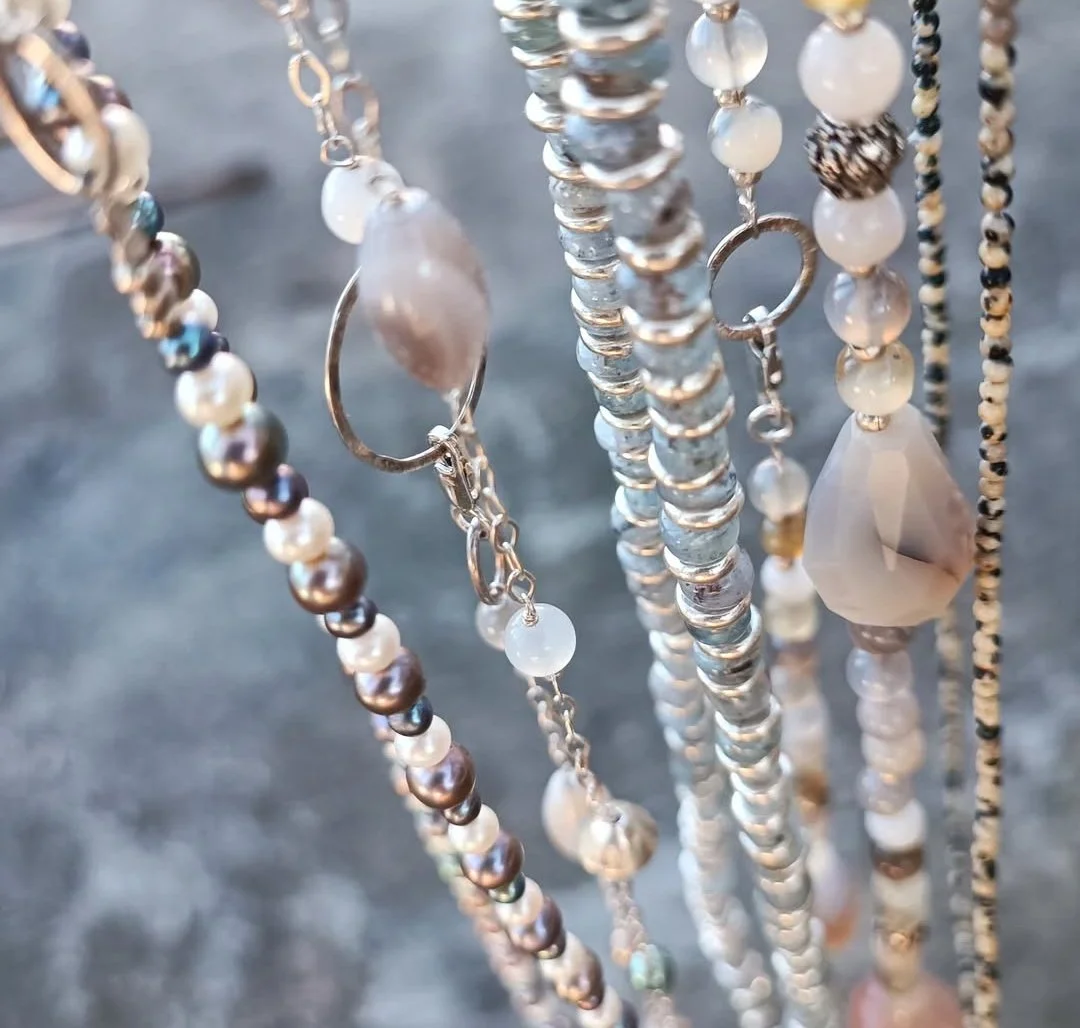 Close-up of various beaded jewelry and necklaces hanging, including pearl, glass, and gemstone beads.