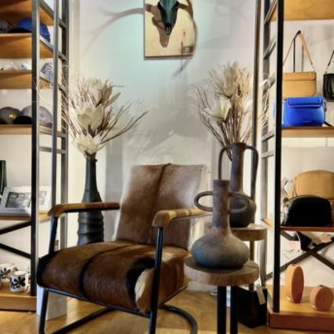 Living room corner with mid-century modern leather armchair, decorative vases with dried flowers, and metal shelving units with assorted decor items, bookshelf, and a painting of a horse's head hanging on a light blue wall.