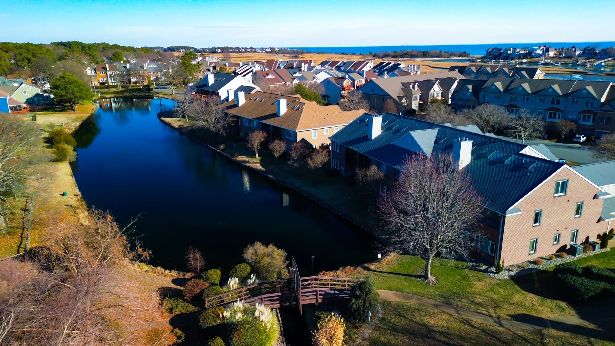 Aerial view of a residential neighborhood with a creek, houses, and a view of the ocean in the background.