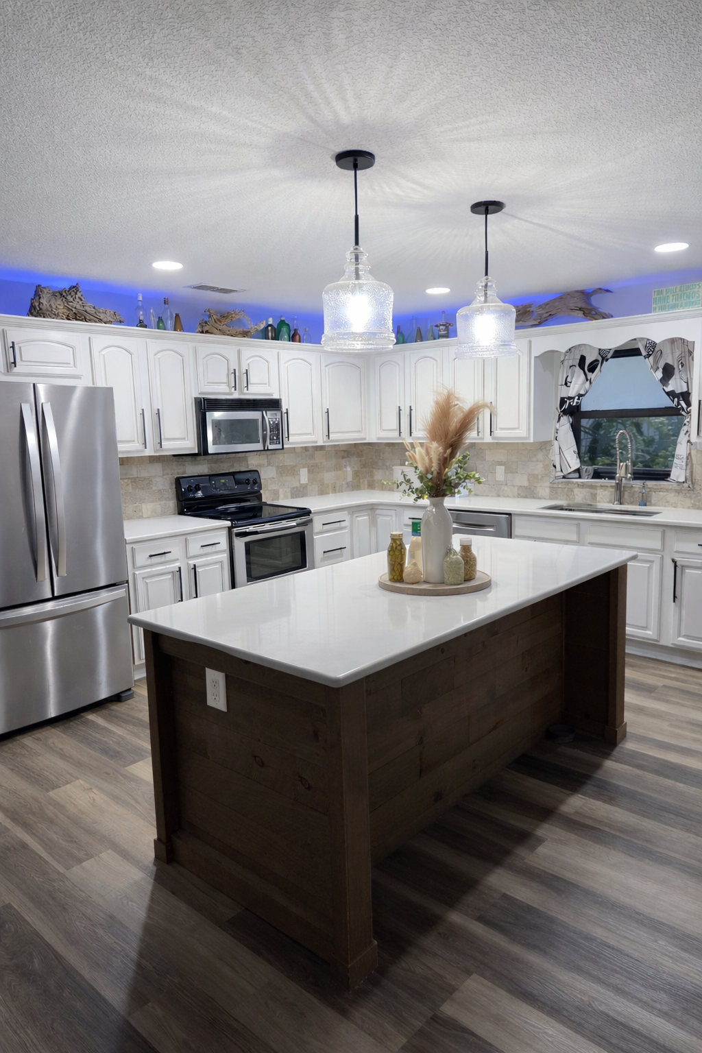 Custom kitchen remodel featuring a quartz island, white cabinetry, tile backsplash, pendant lighting, and luxury vinyl flooring