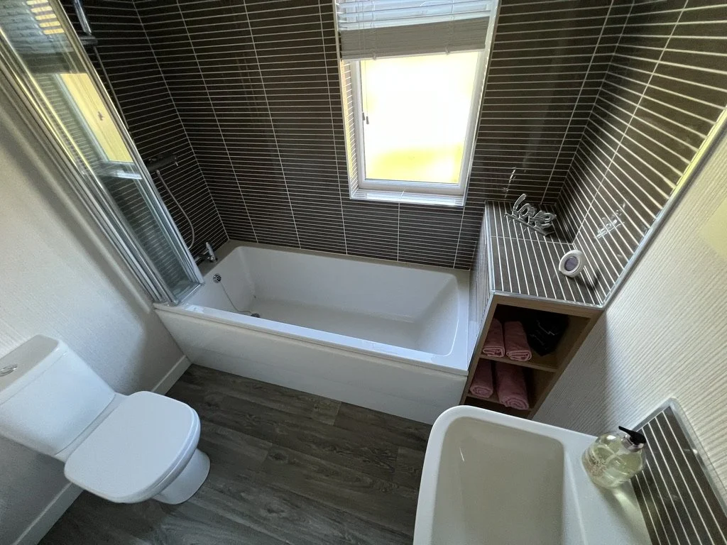 Bathroom with a bathtub beneath a window, a toilet, a sink, and shelves with towels.