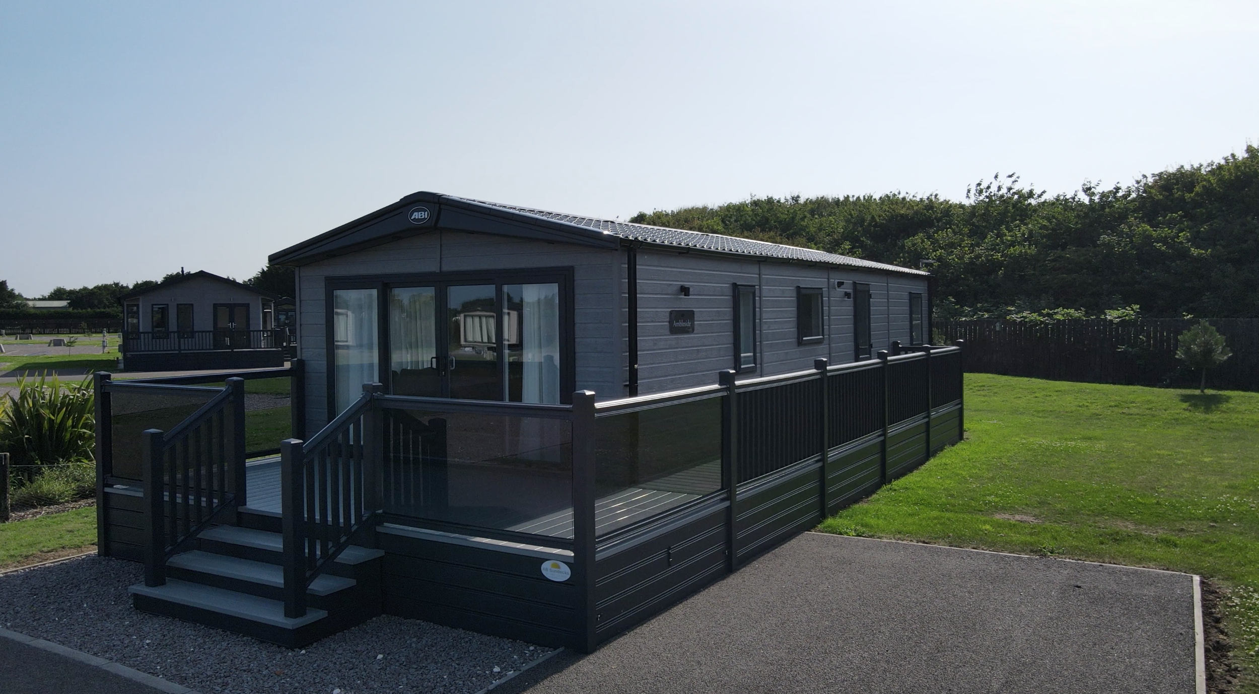 the ABI Premier lodge with light grey cladding and a large deck with glass banisters, sited at the woodlands lodge park skegness