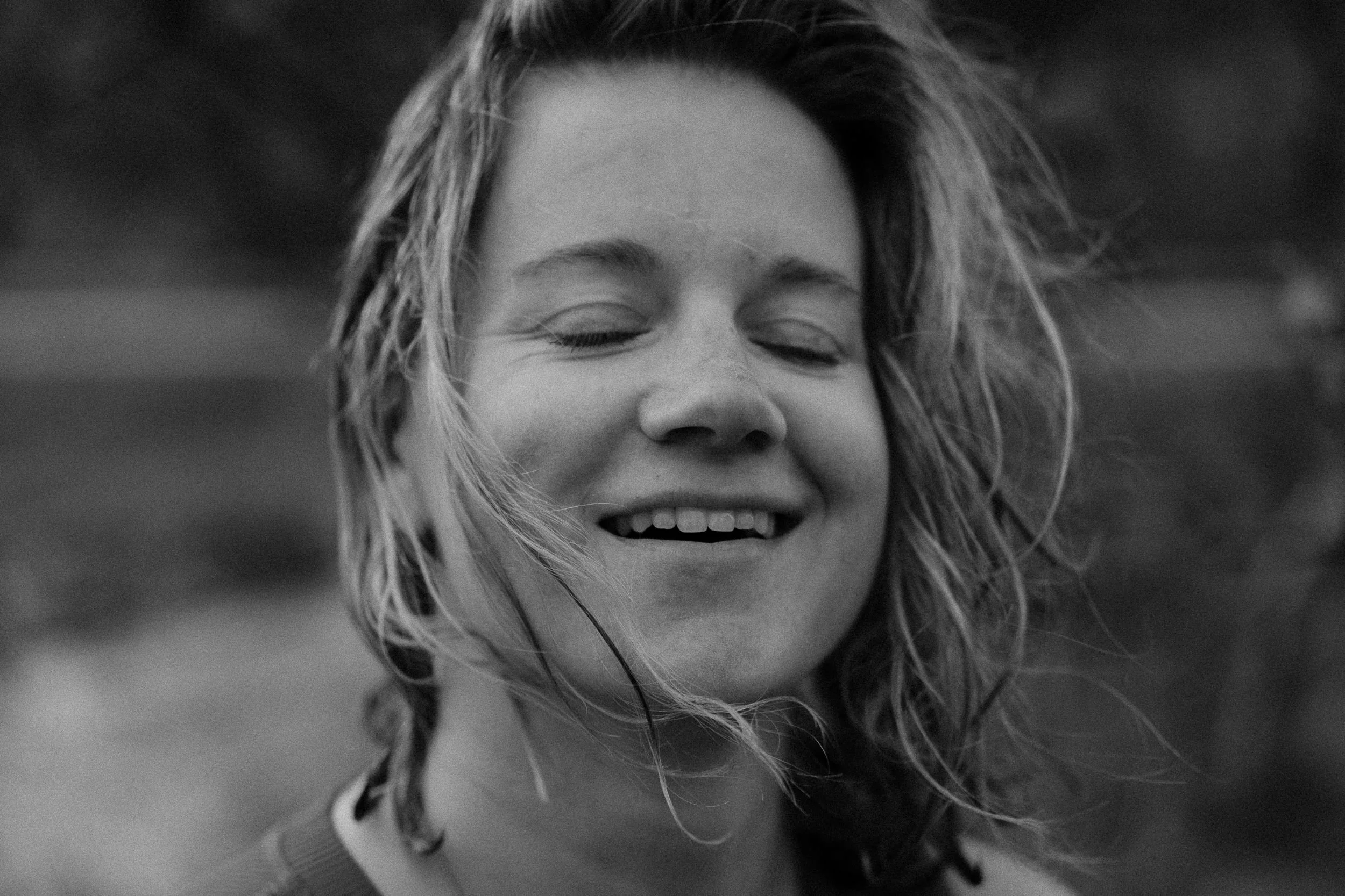 Black and white close-up portrait of laughing woman with wind-blown hair, arctic Norway editorial photography by Tori Pintar