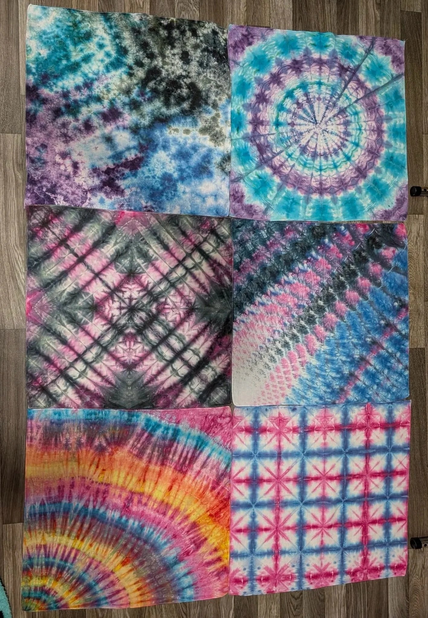 Six tie-dyed bandanas with various colorful patterns laid out on a wooden floor.